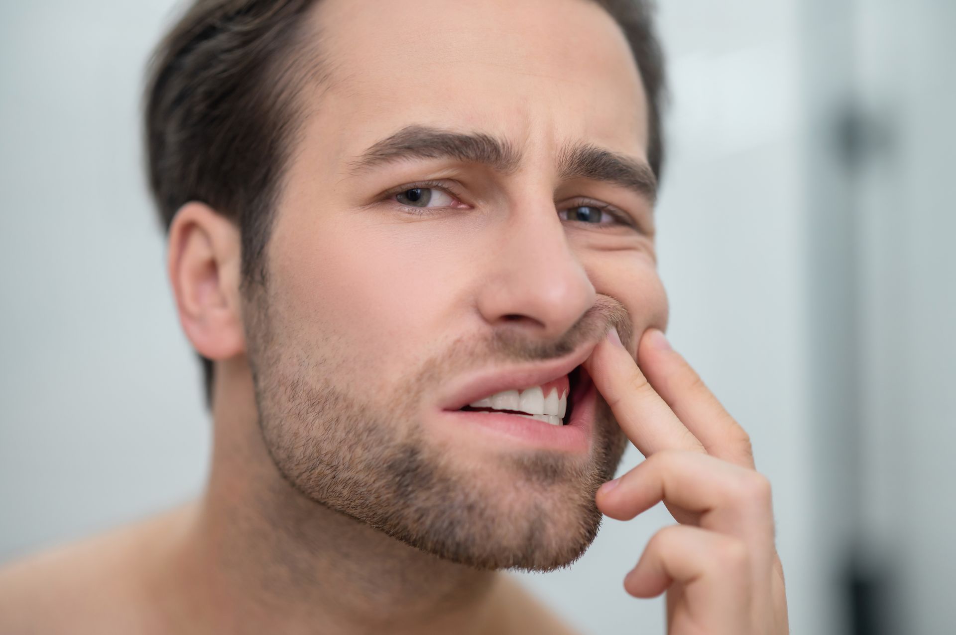 A man with a beard is holding his mouth in pain.