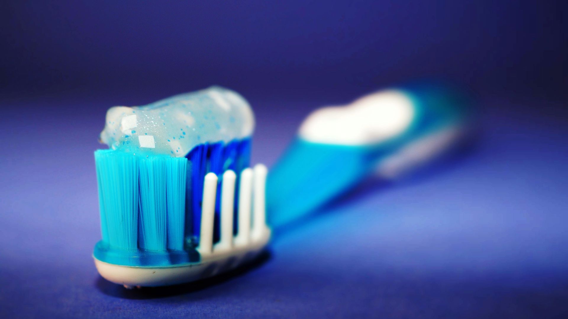 A blue toothbrush with toothpaste on it on a blue surface.