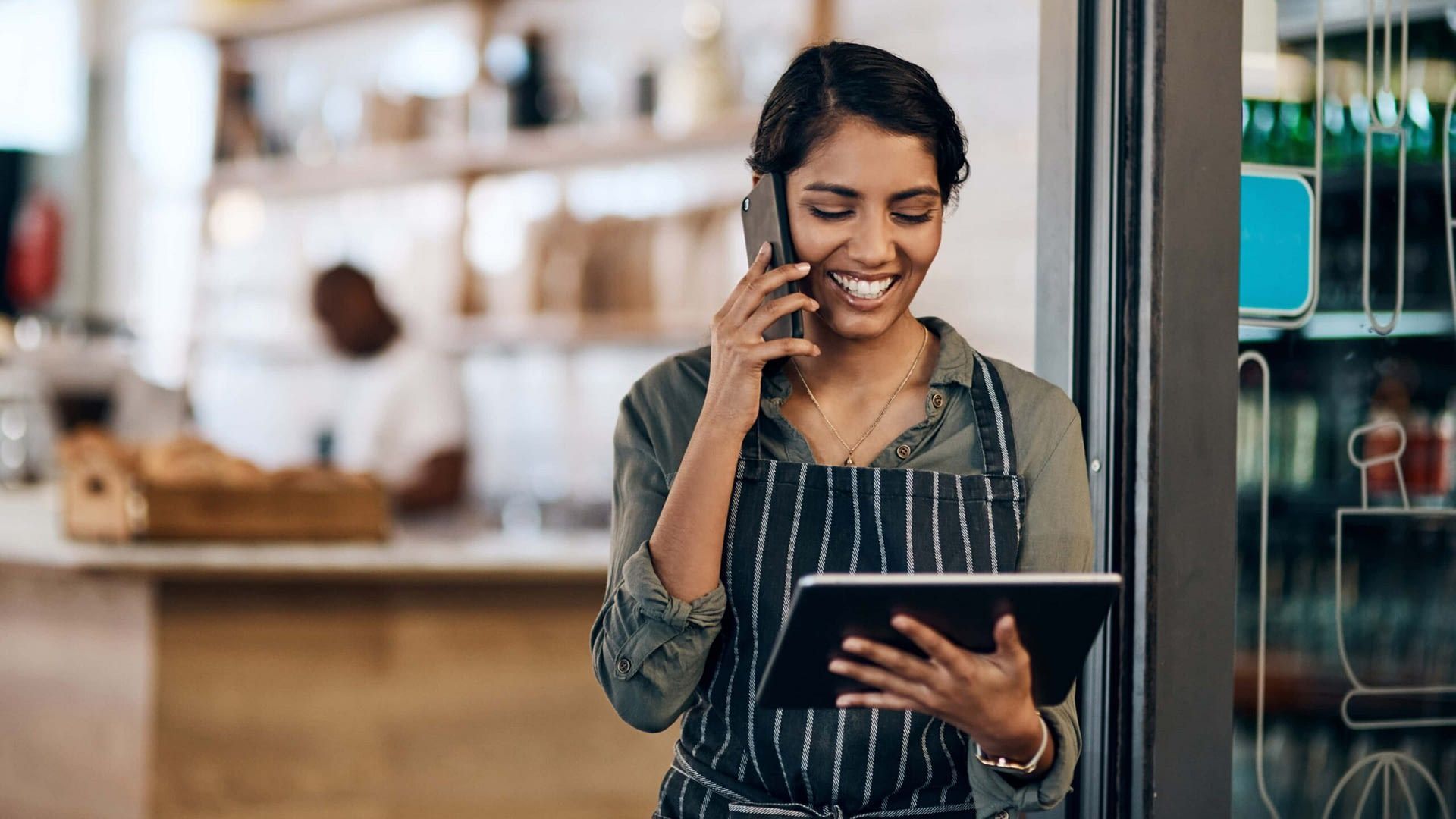 A woman is talking on a cell phone while holding a tablet.