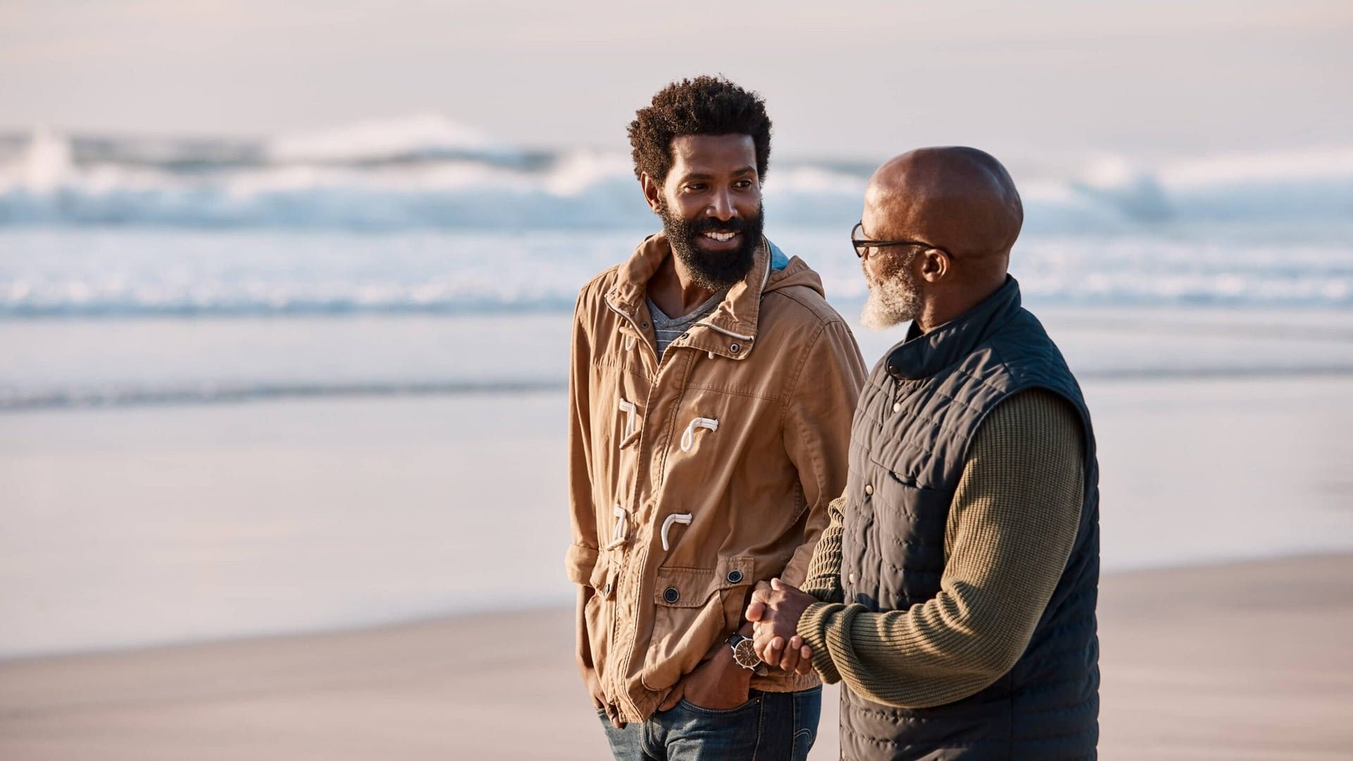 older African-American man walking on beach having a talk with his adult son