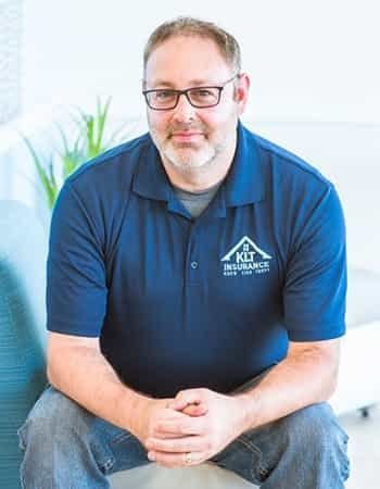 A man wearing glasses and a blue shirt is sitting on a couch.