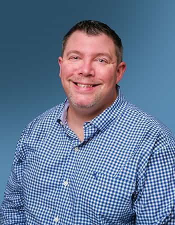 A man in a blue plaid shirt is smiling for the camera.