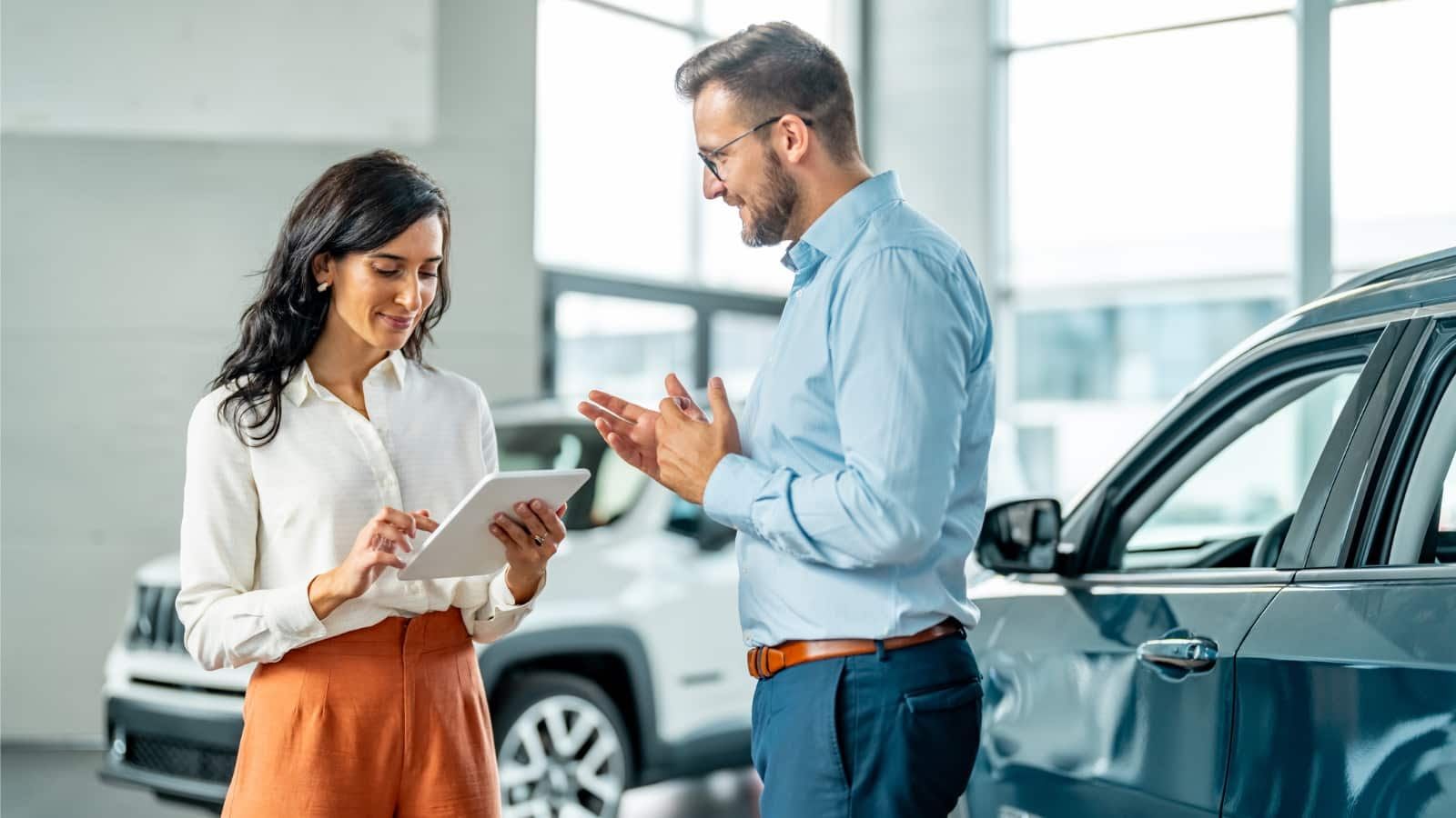 A man and a woman are looking at a tablet in a car showroom.