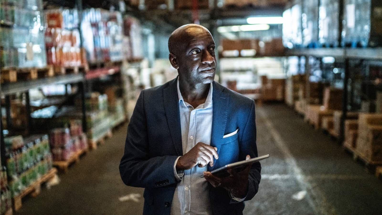 A man in a suit is using a tablet in a warehouse.