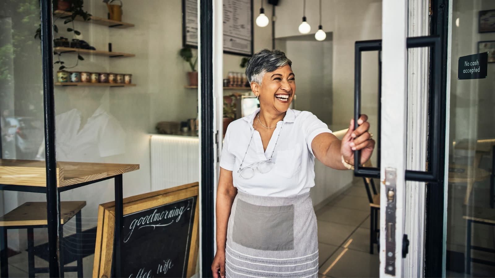 A woman is opening the door of a restaurant.