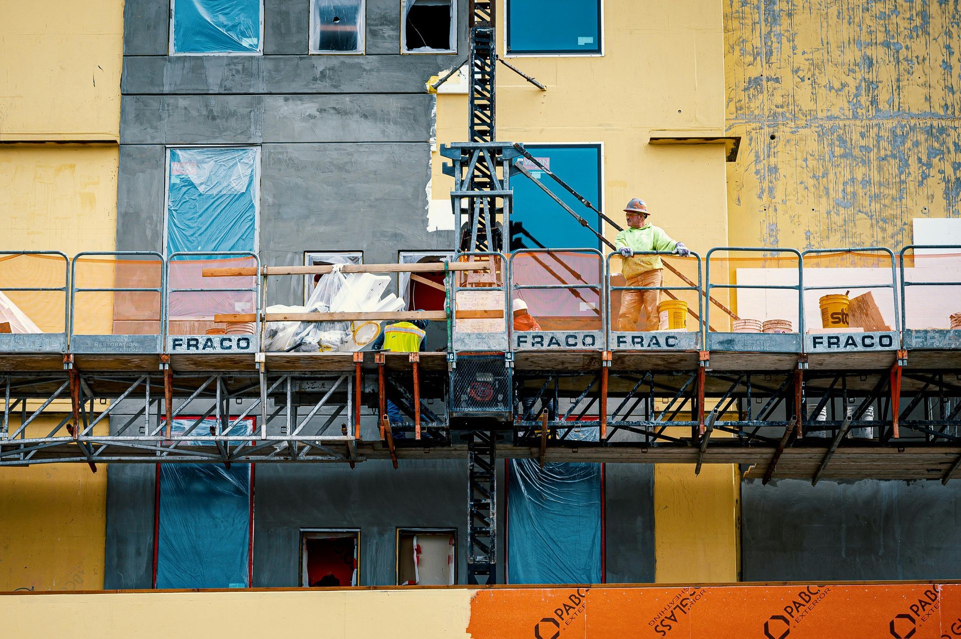 A man is standing on a scaffolding in front of a building under construction.