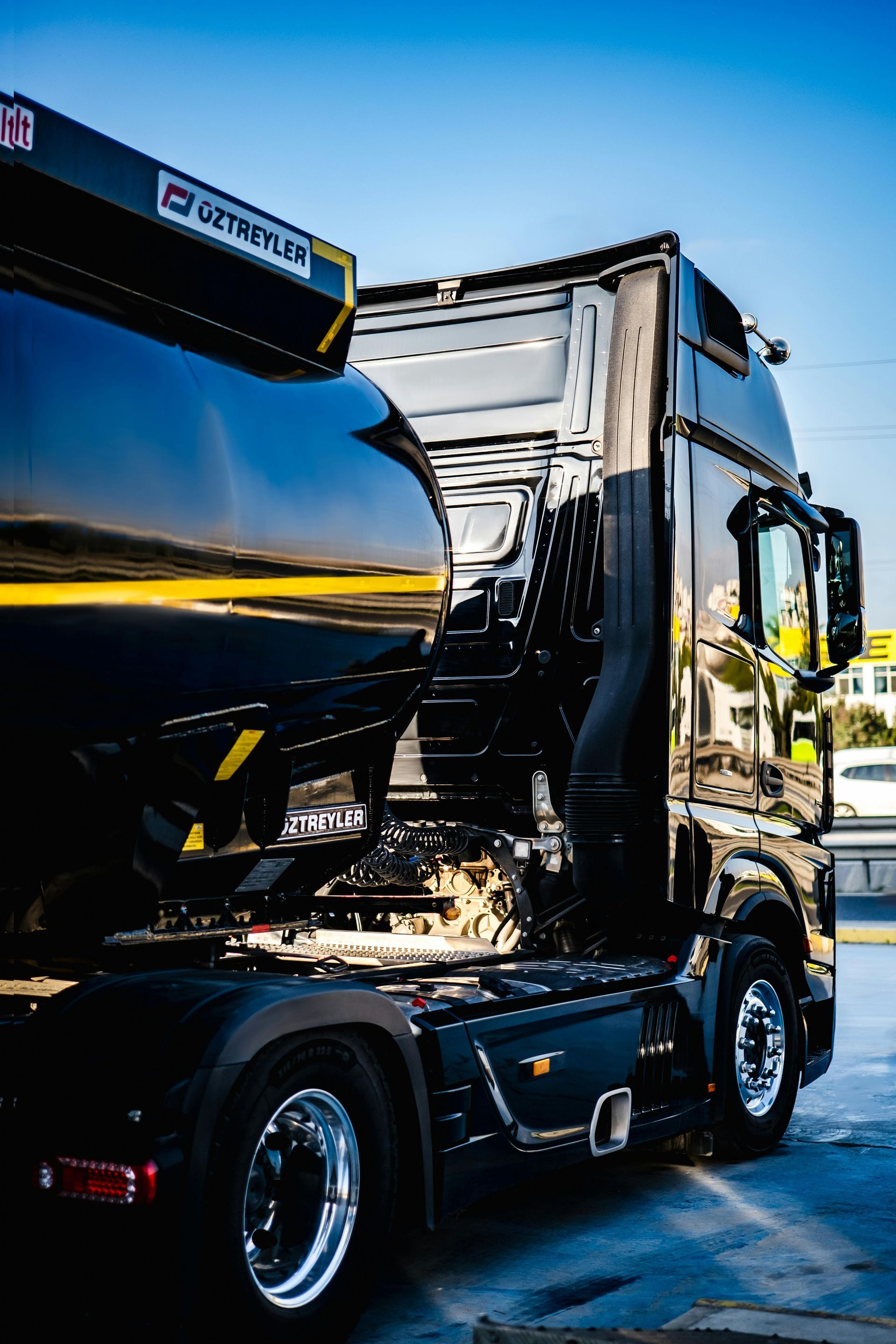 A black semi truck with a crane on the back is parked in a parking lot.