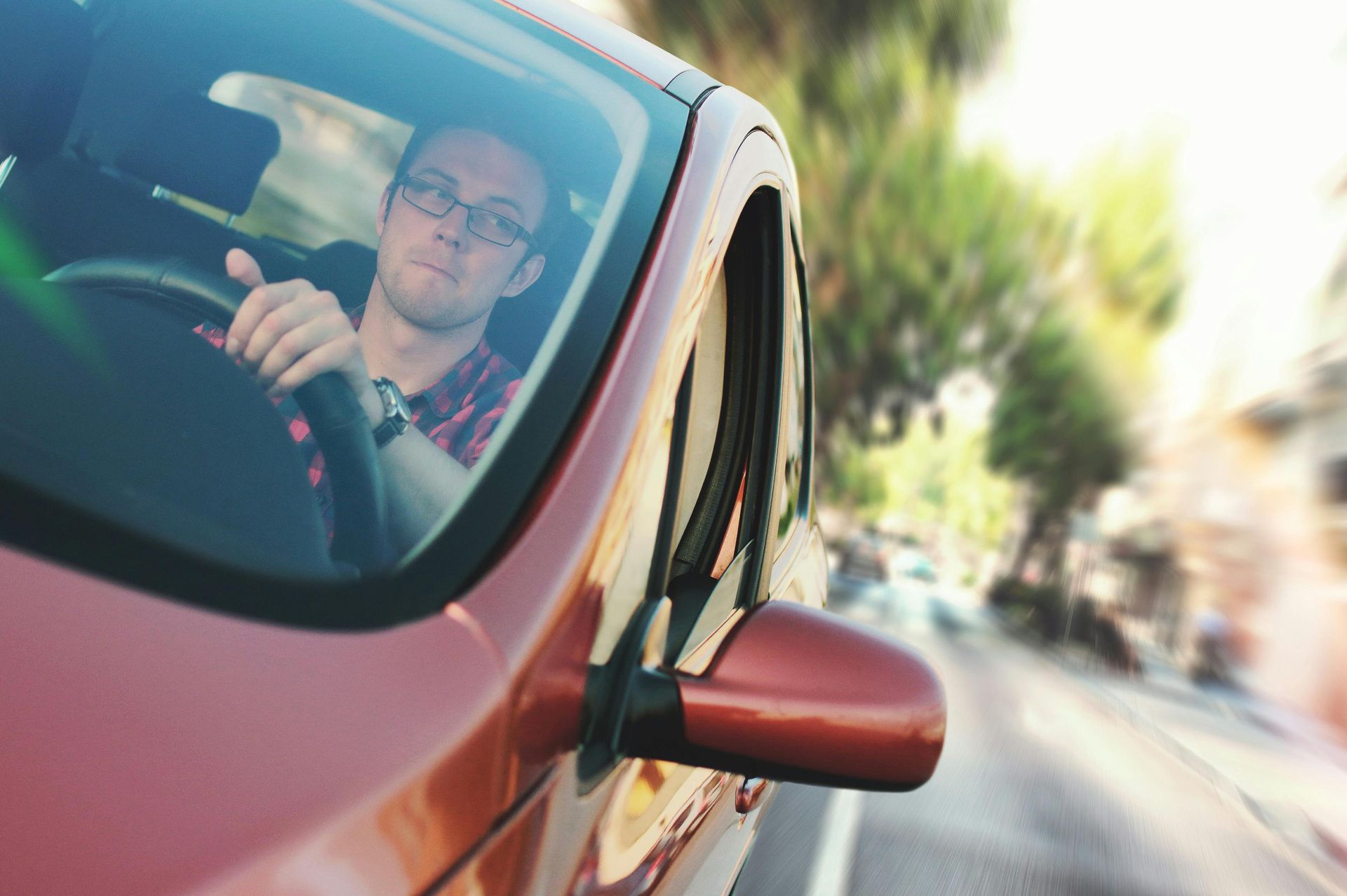 A man is driving a red car down a city street.