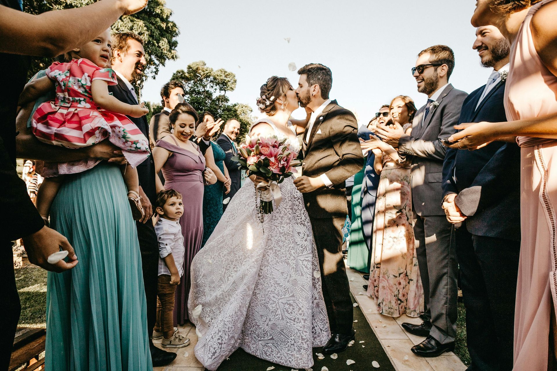 A bride and groom are kissing in front of their wedding guests.