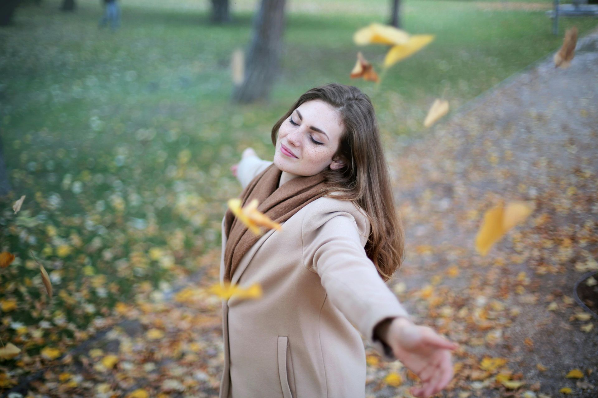 A woman is throwing leaves in the air in a park.