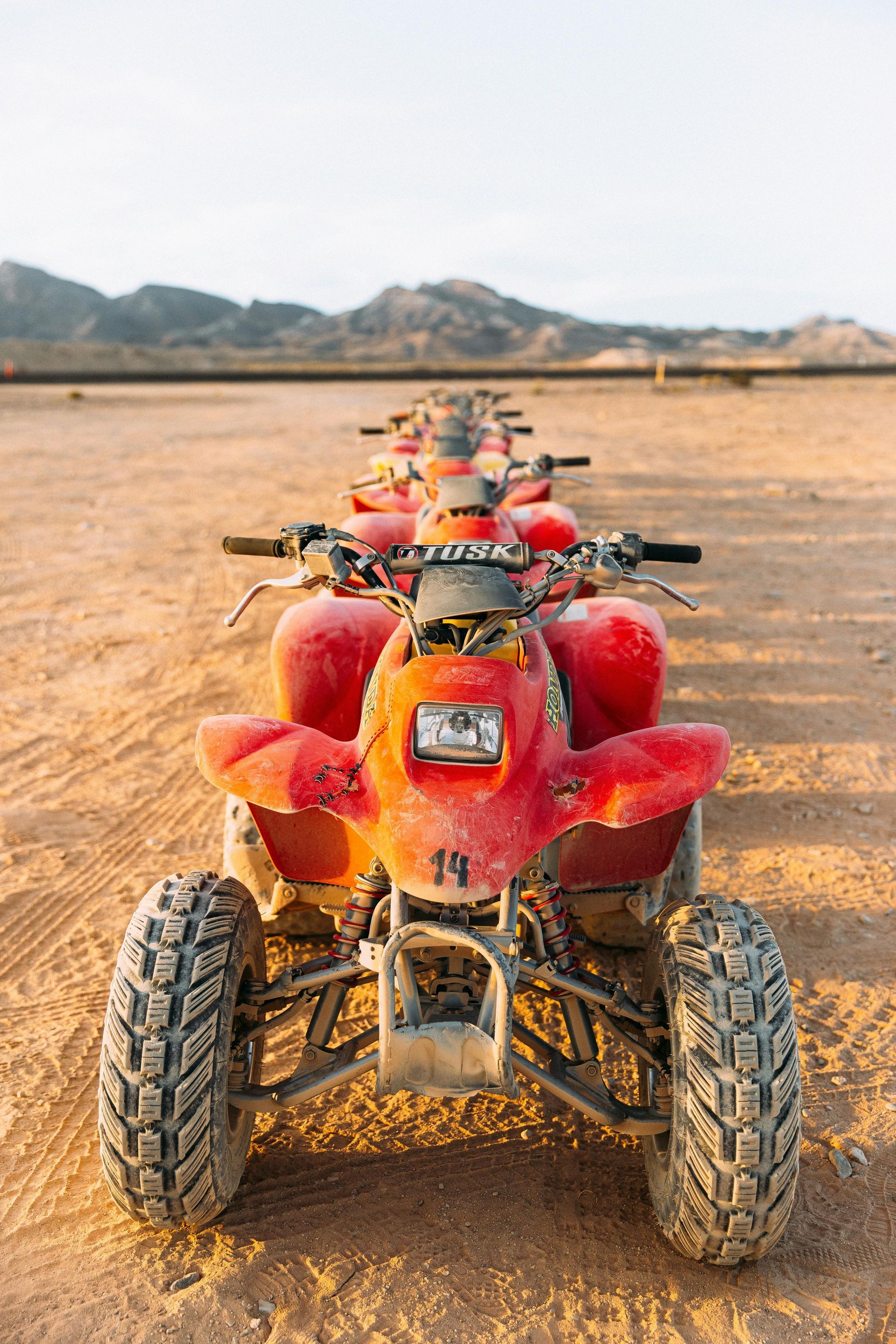 A row of red atvs are parked in the desert.