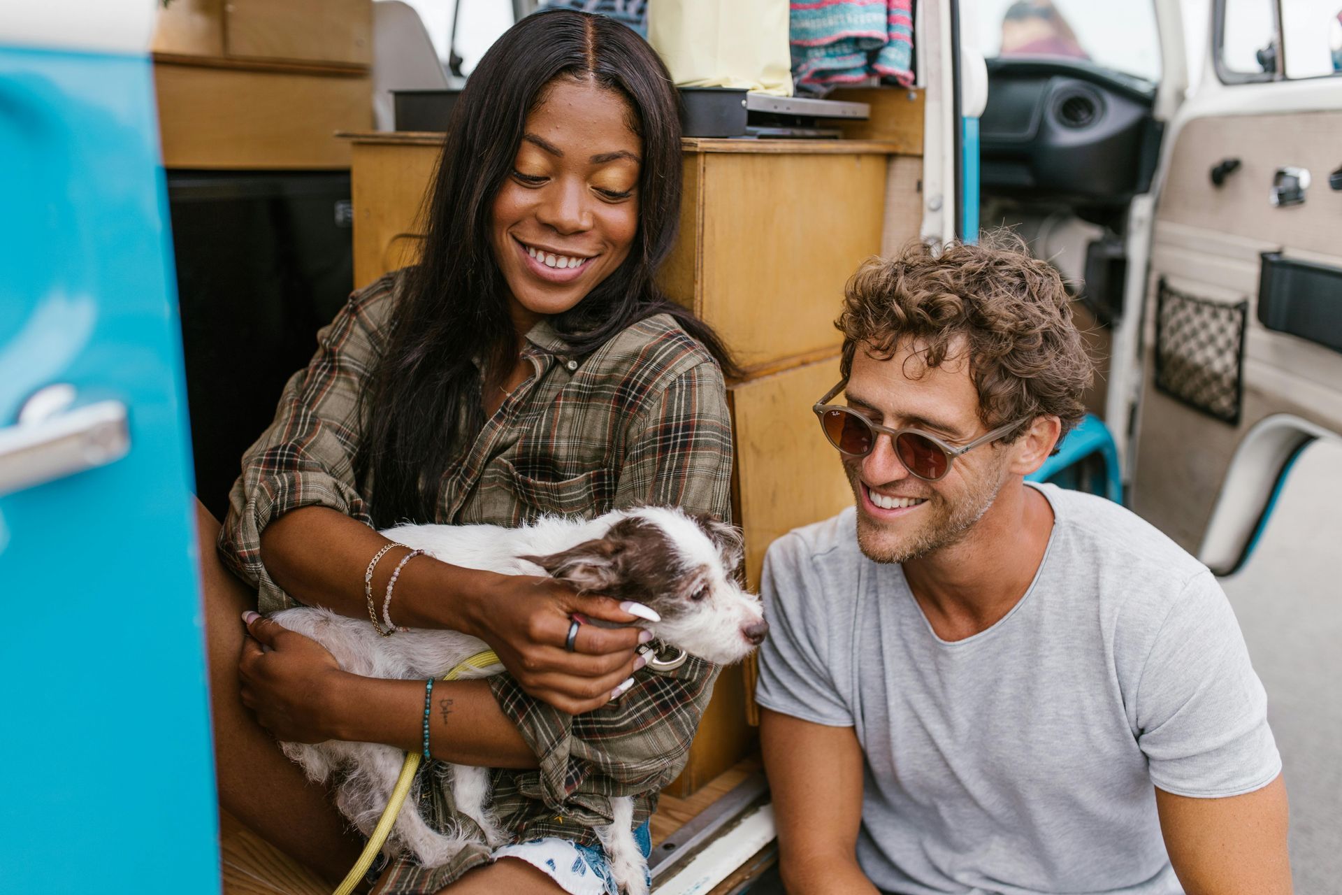 A man and a woman are sitting in the back of a van holding a dog.