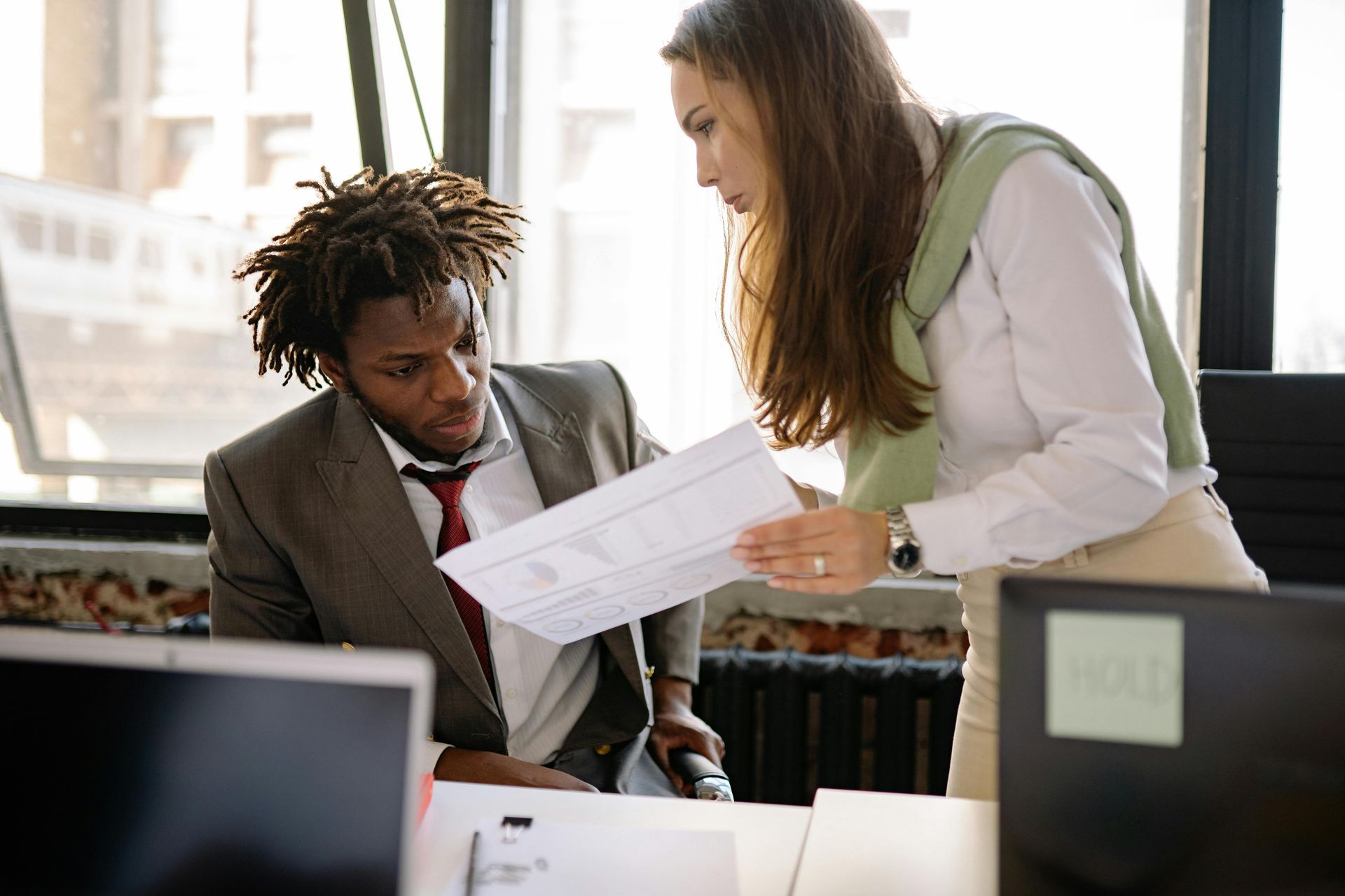 A man and a woman are looking at a piece of paper in an office.