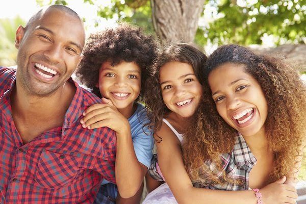 A family is sitting under a tree and smiling for the camera.