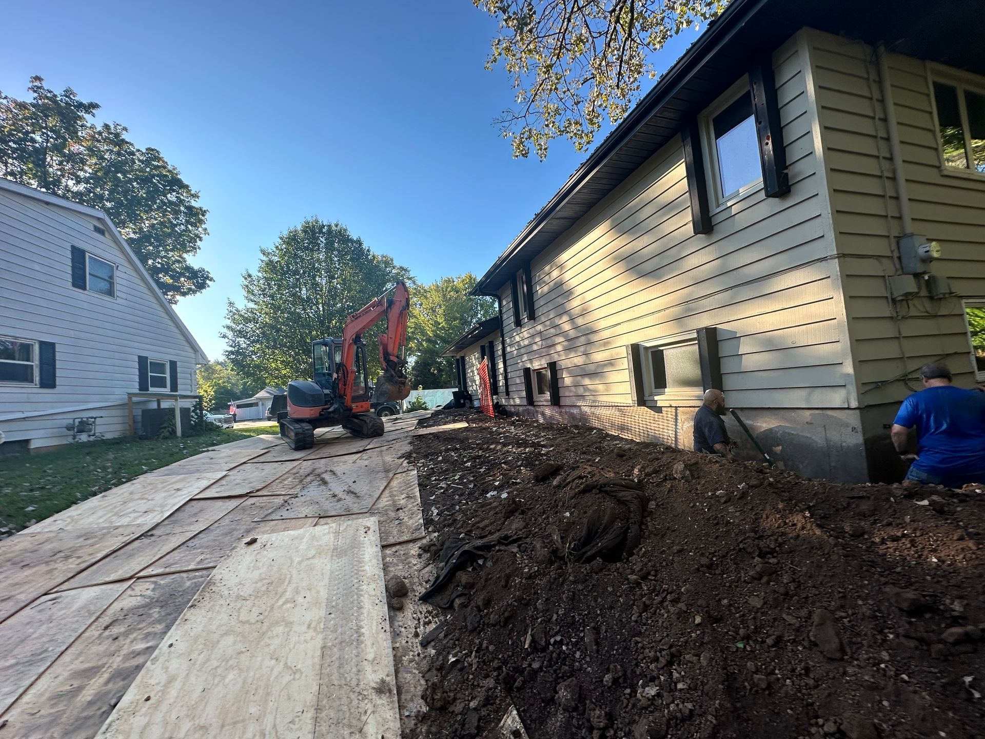 An excavator is digging a hole in front of a house.