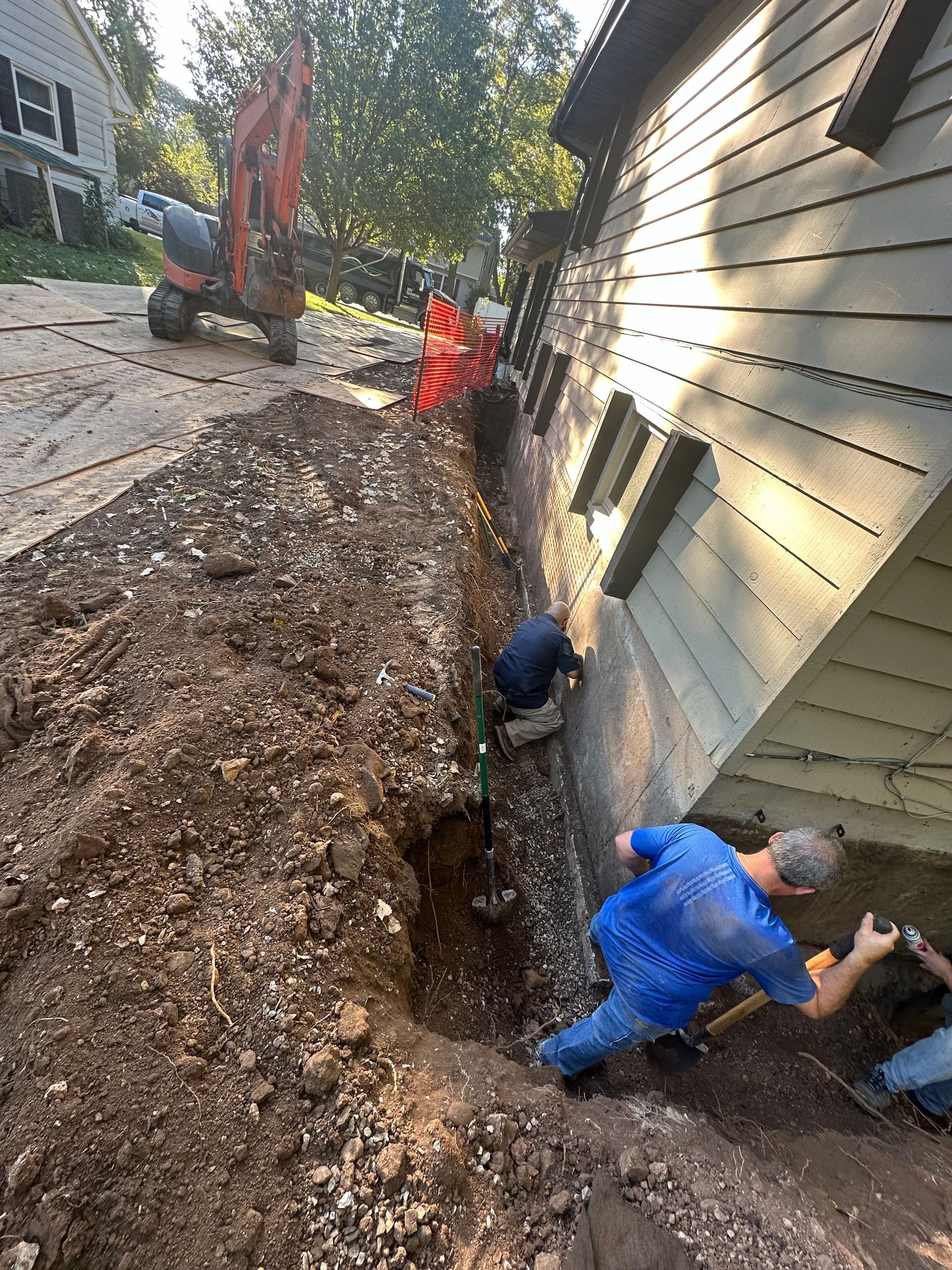 A man is digging a hole in the ground in front of a house.