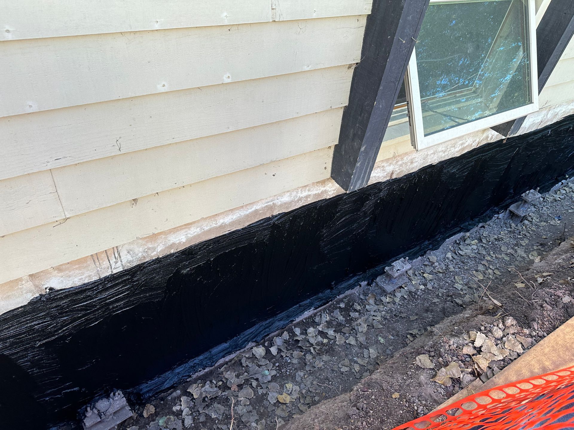 A house is being waterproofed with black paint.