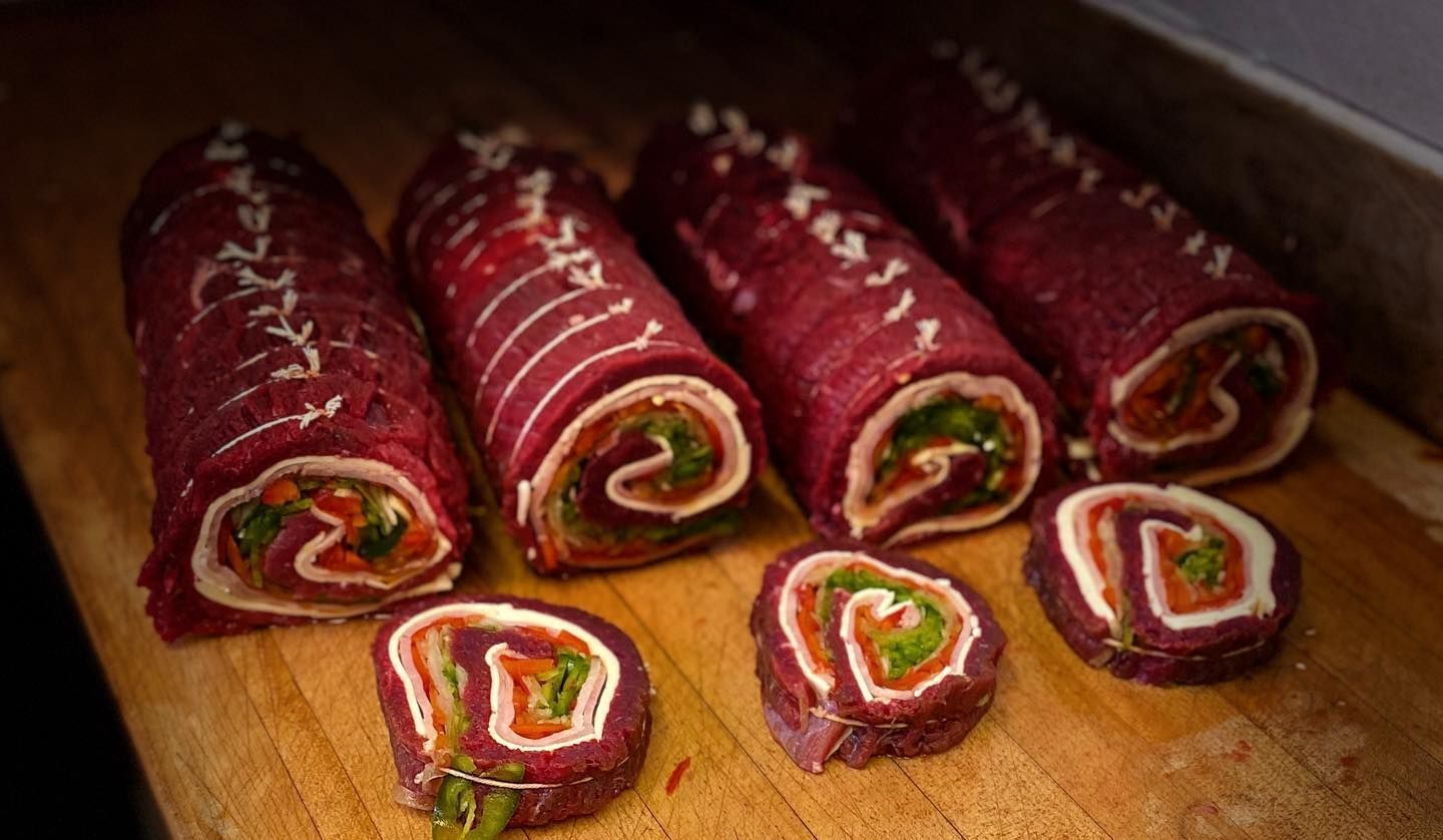 Une planche à découper en bois surmontée de rouleaux de viande et de légumes.