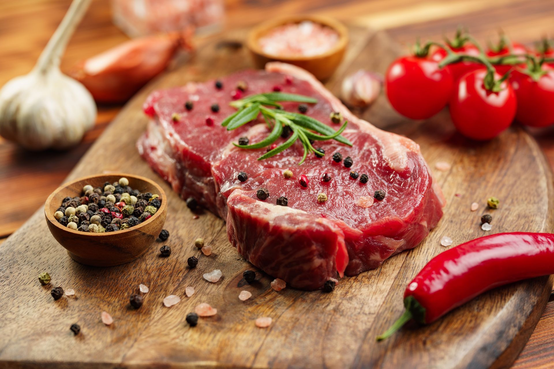 Un steak cru est posé sur une planche à découper en bois entouré de légumes et d'épices.