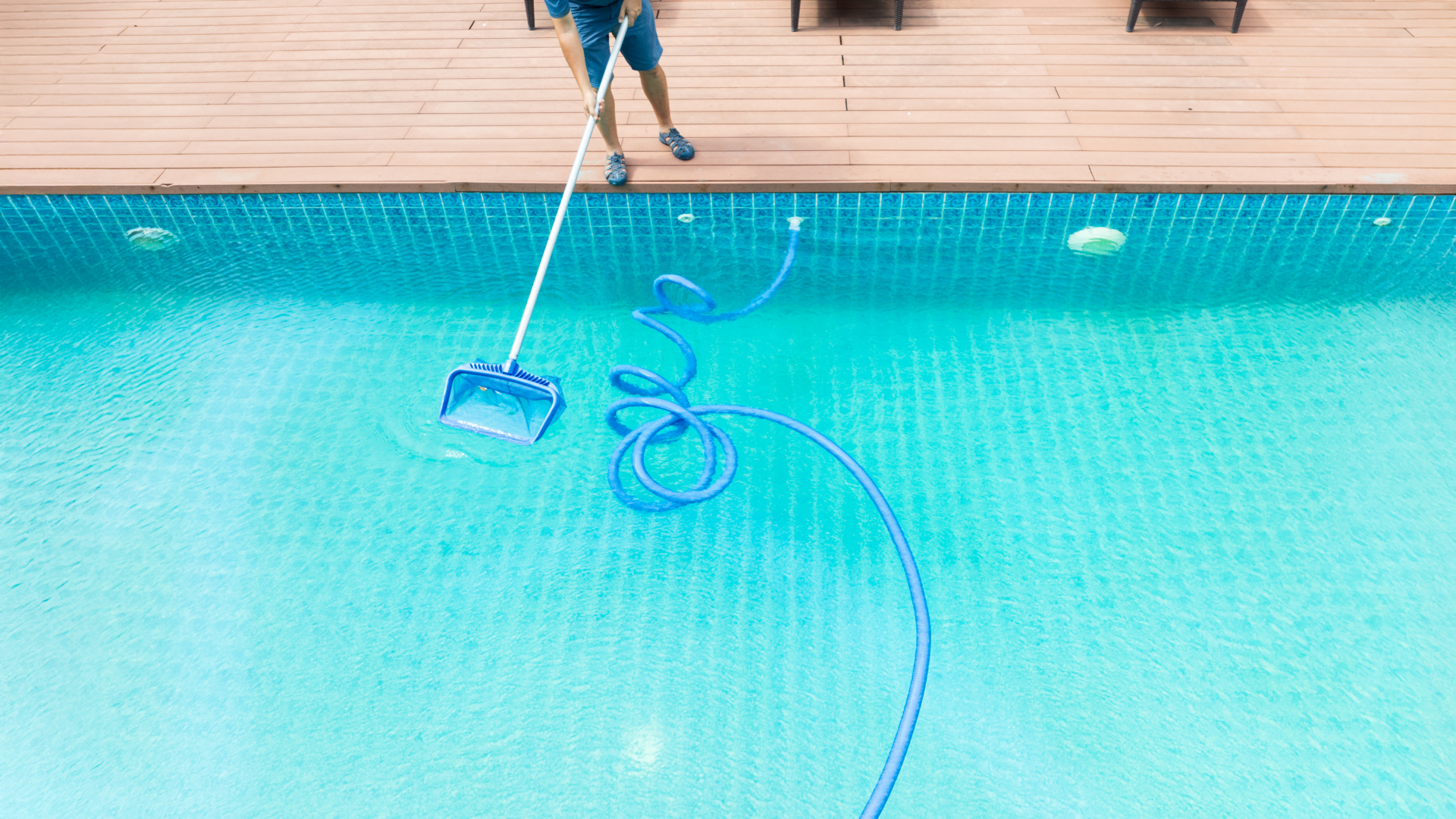 Hands holding a pool test strip next to a matching color chart bottle against a blurred blue water background.