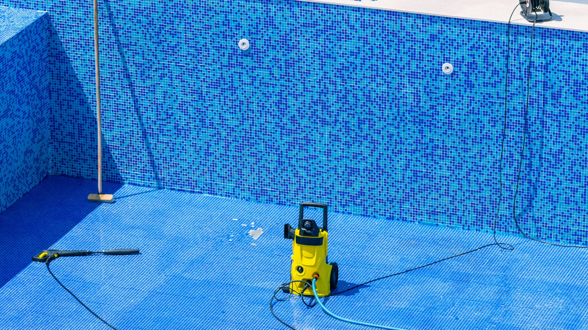 A technician in a red shirt repairs pool plumbing equipment inside an open utility pit on a pool deck.