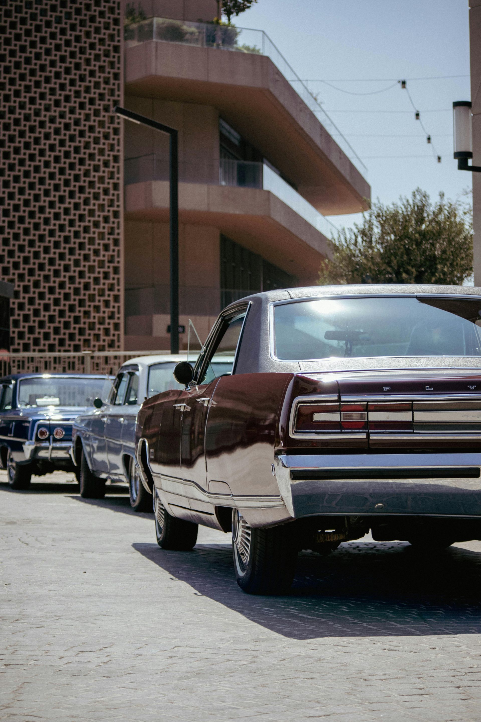 Classic cars parked on a street beside a modern building under a clear sky