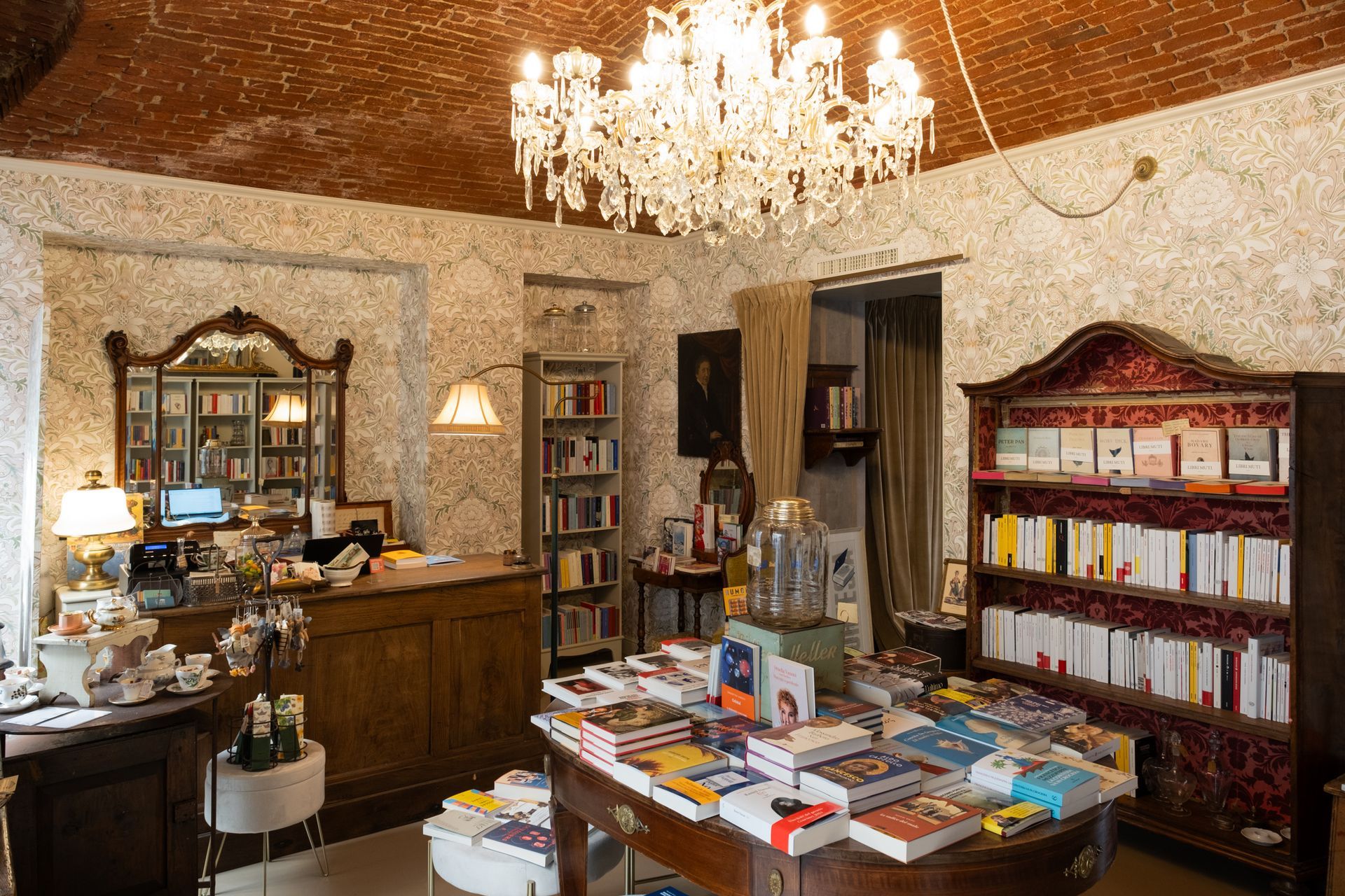 Elegante interno di un negozio di antiquariato con lampadario, mobili in legno e libri esposti su un tavolo centrale.