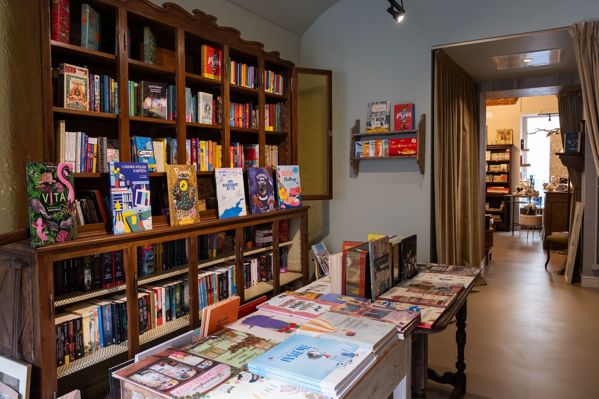 Interno di una libreria con scaffali in legno, libri colorati e un tavolo espositivo in uno stretto corridoio.
