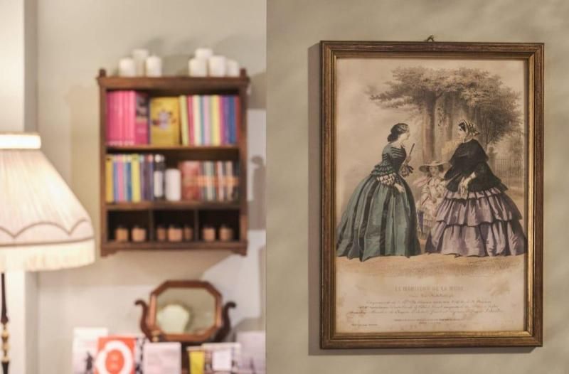 Un disegno incorniciato in stile vintage è appeso a una parete beige, accanto a una piccola libreria e a una lampada.