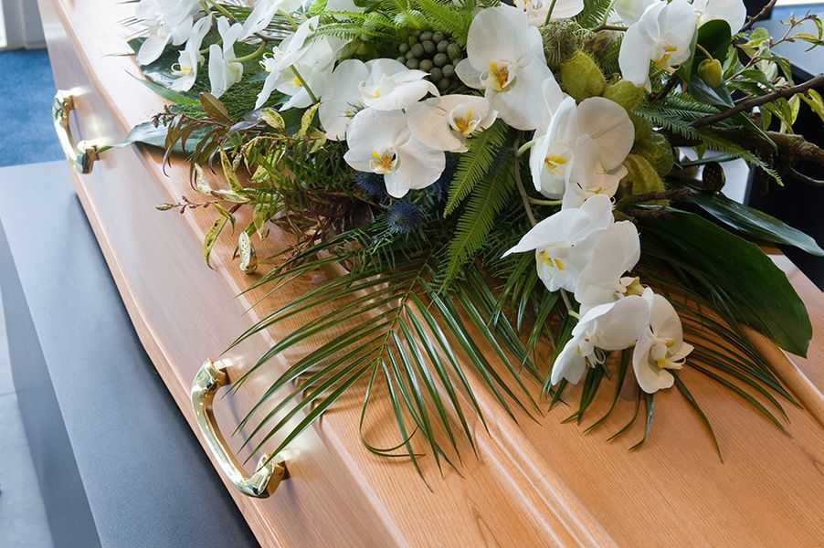 A coffin with white flowers and green leaves on it.