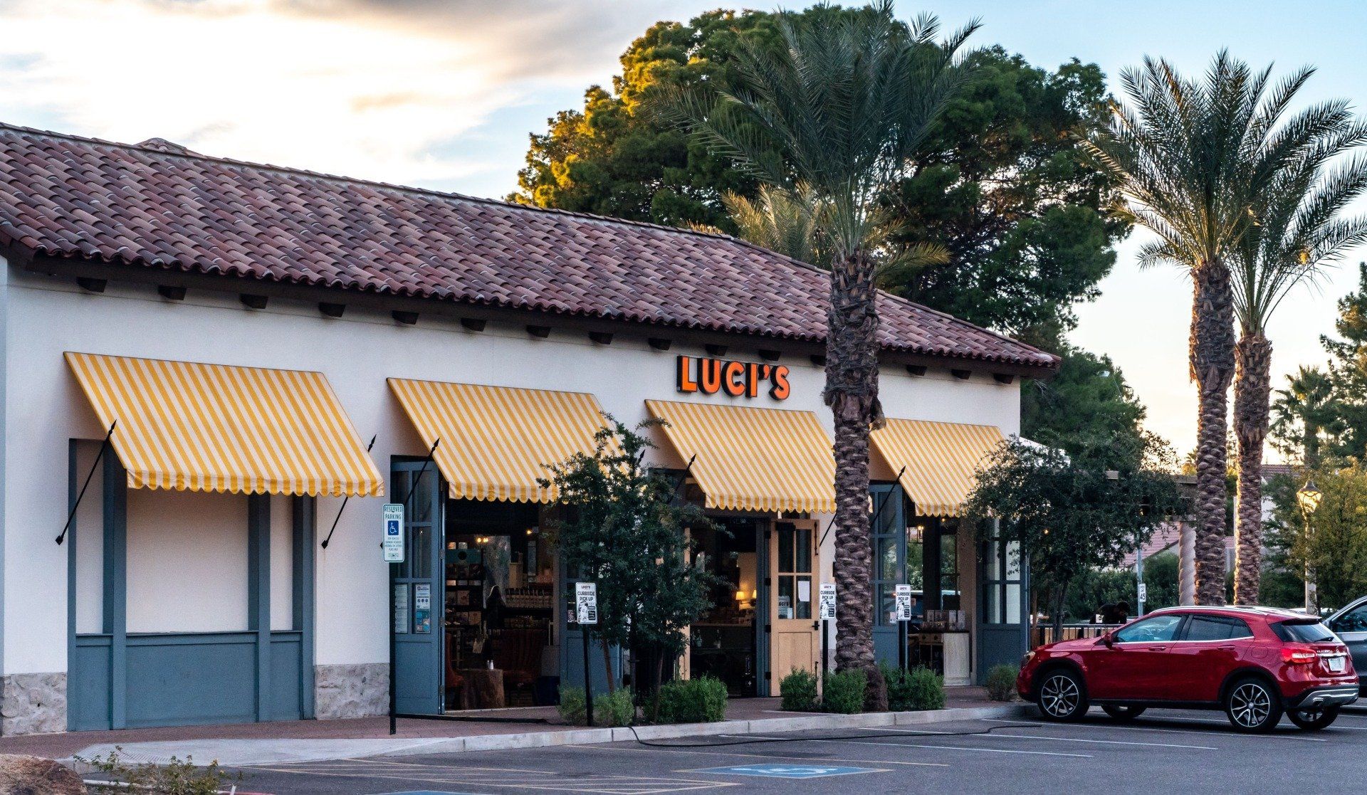 A red car is parked in front of a restaurant called rick 's