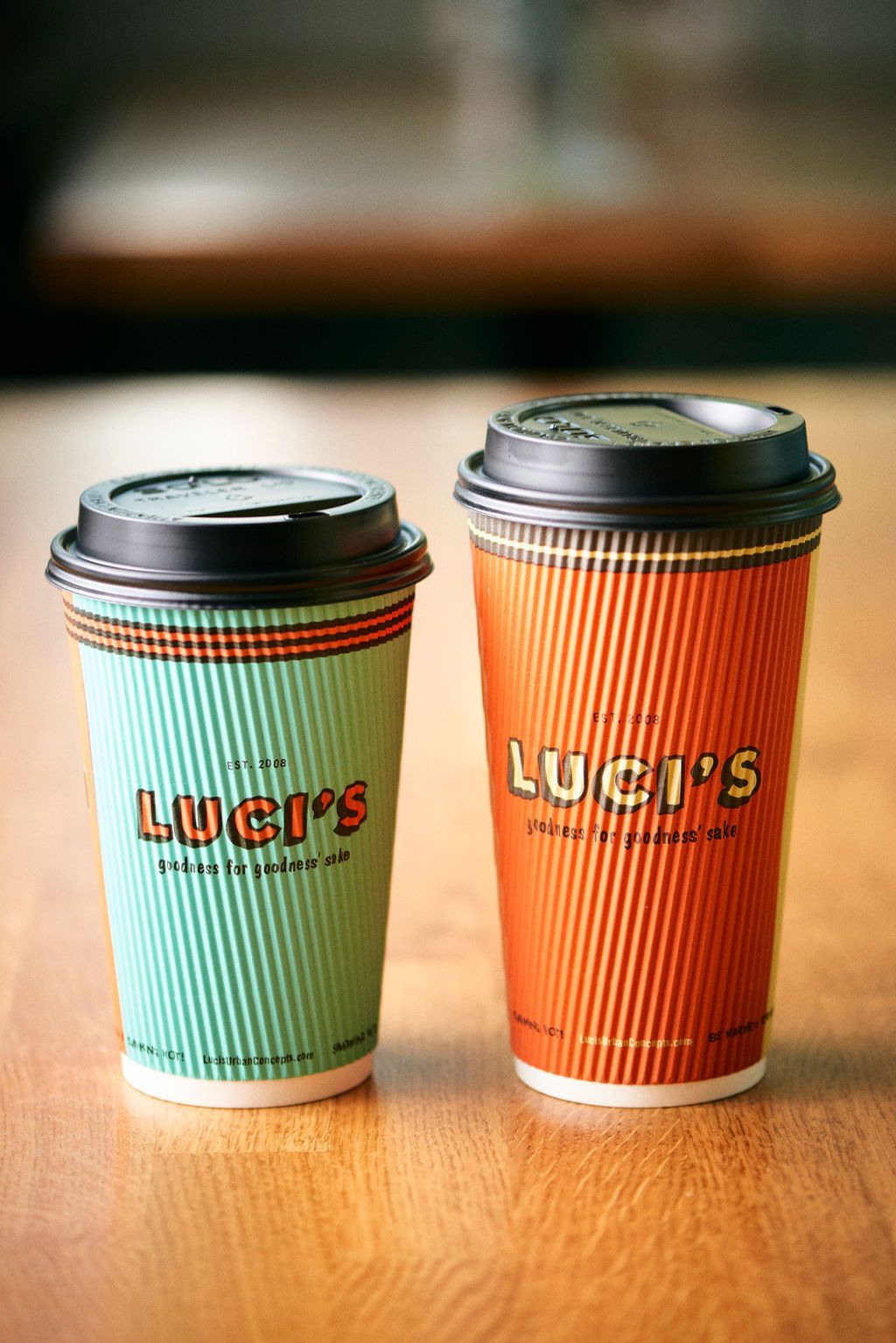 Two cups of coffee from luci 's are sitting on a wooden table.