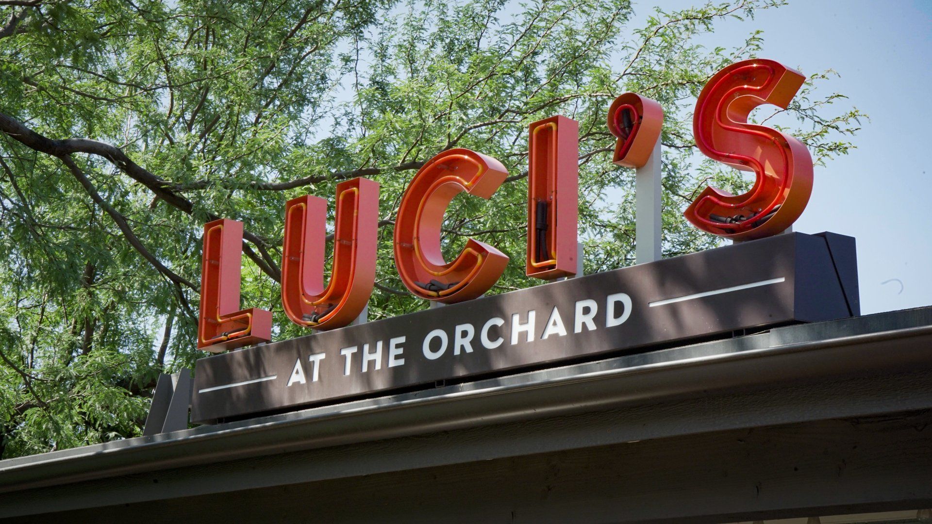 A sign for luci 's at the orchard with trees in the background