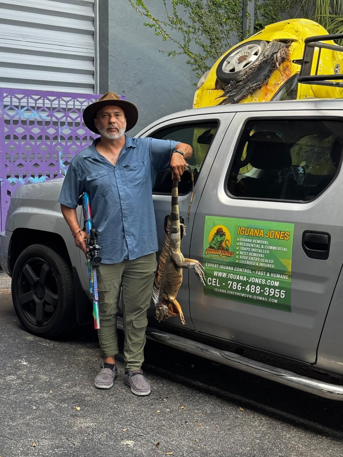 Man holding iguana next to a truck with 