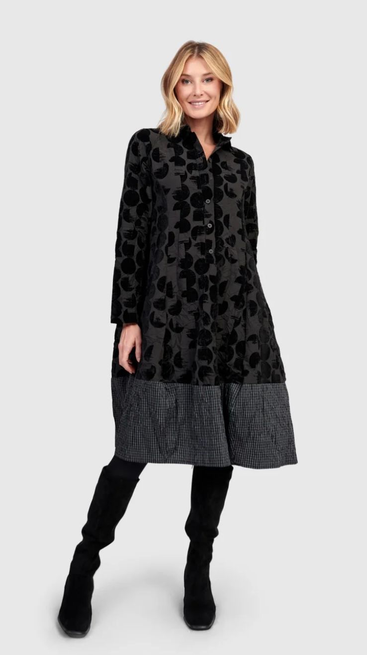 Woman wearing a black floral coat, boots, standing, smiling.