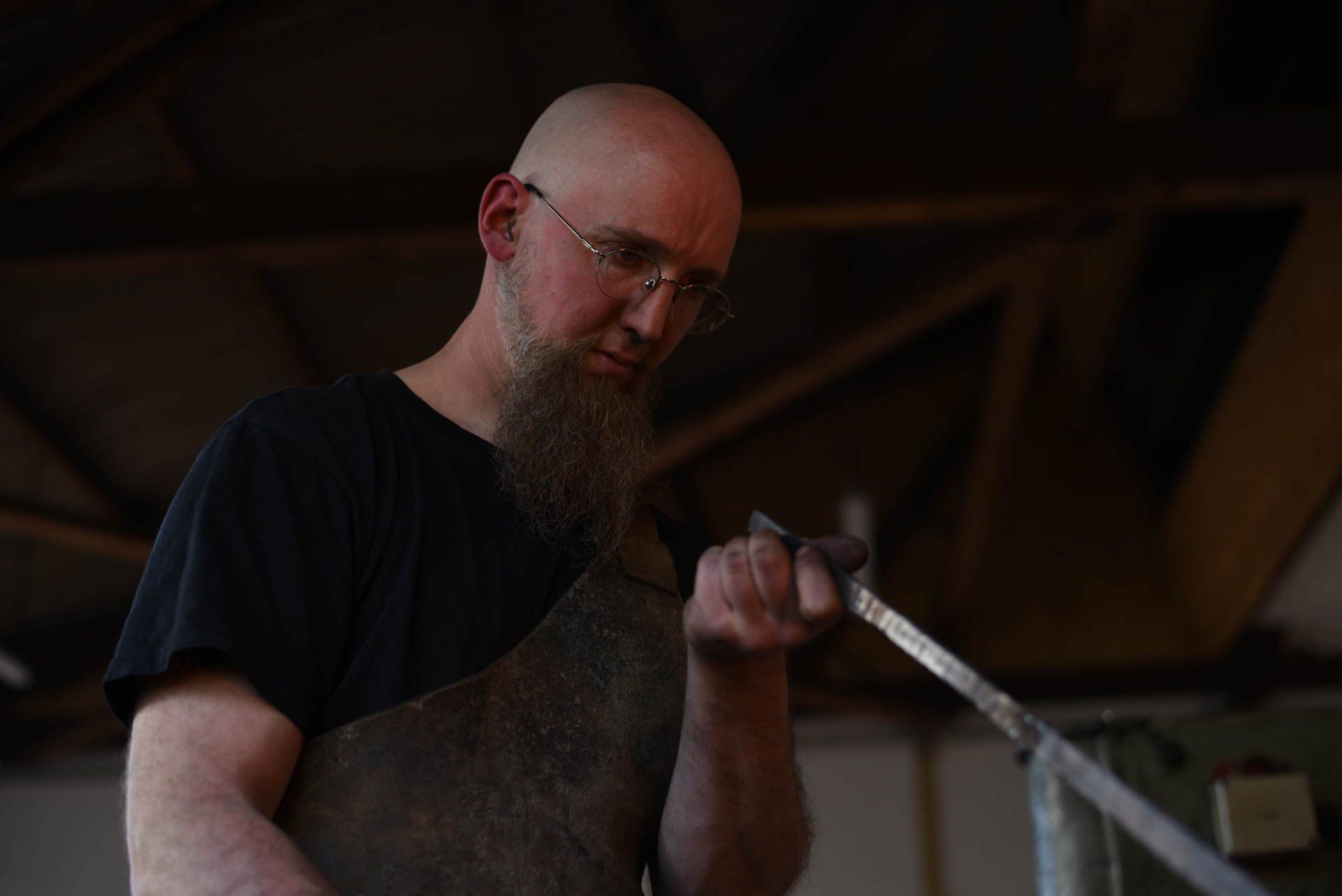 Portrait von Sören Binger bei der Arbeit. Das geschmiedete Stück Stahl wird von ihm in Augenschein genommen und geprüft.