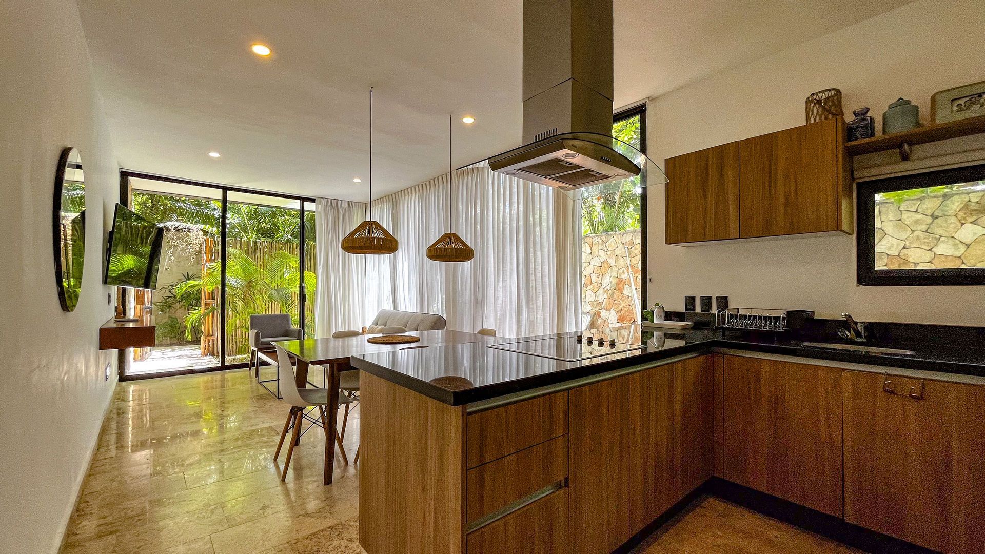 Cocina moderna con muebles de madera, campana de acero inoxidable, mesa de comedor y grandes ventanales.