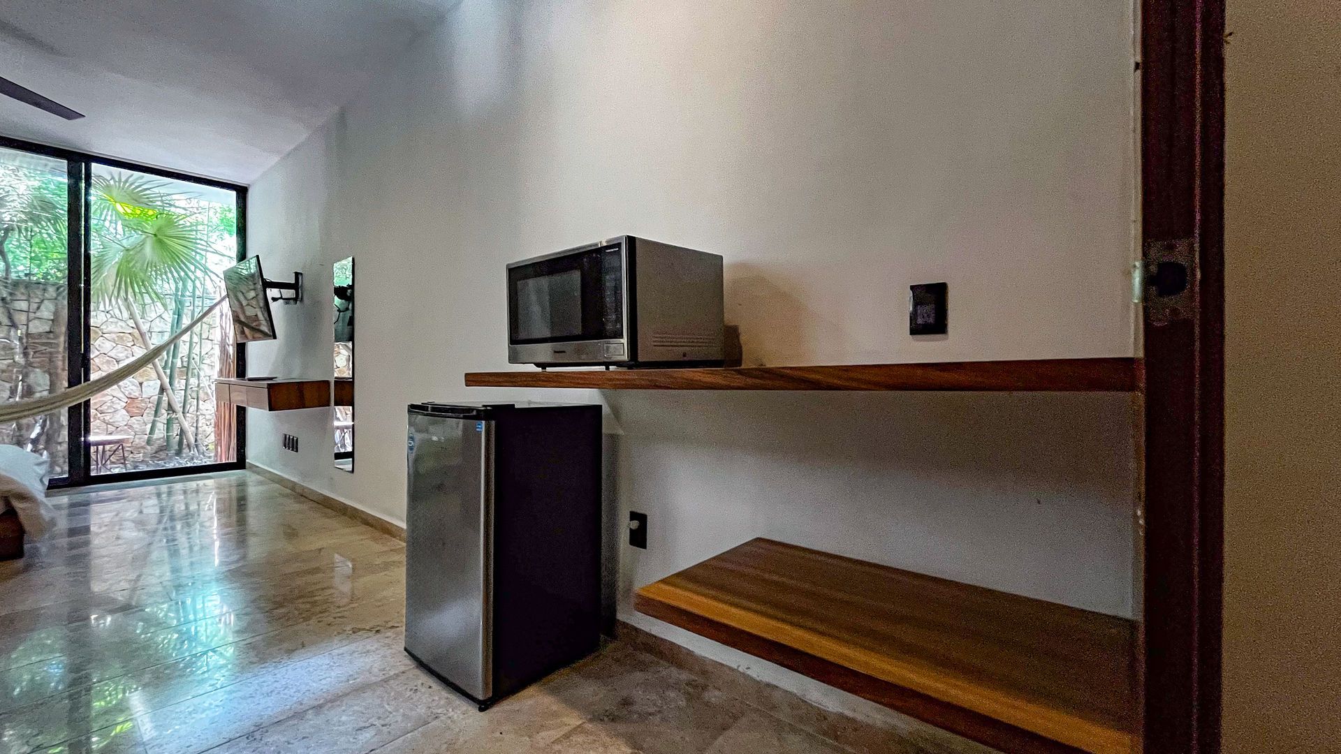 Habitación pequeña con microondas en un estante, mininevera y ventana grande con vista a los árboles.