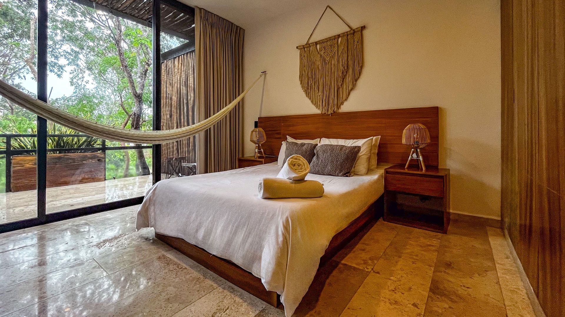 Dormitorio con amplio ventanal, hamaca, cama de madera y decoración natural.