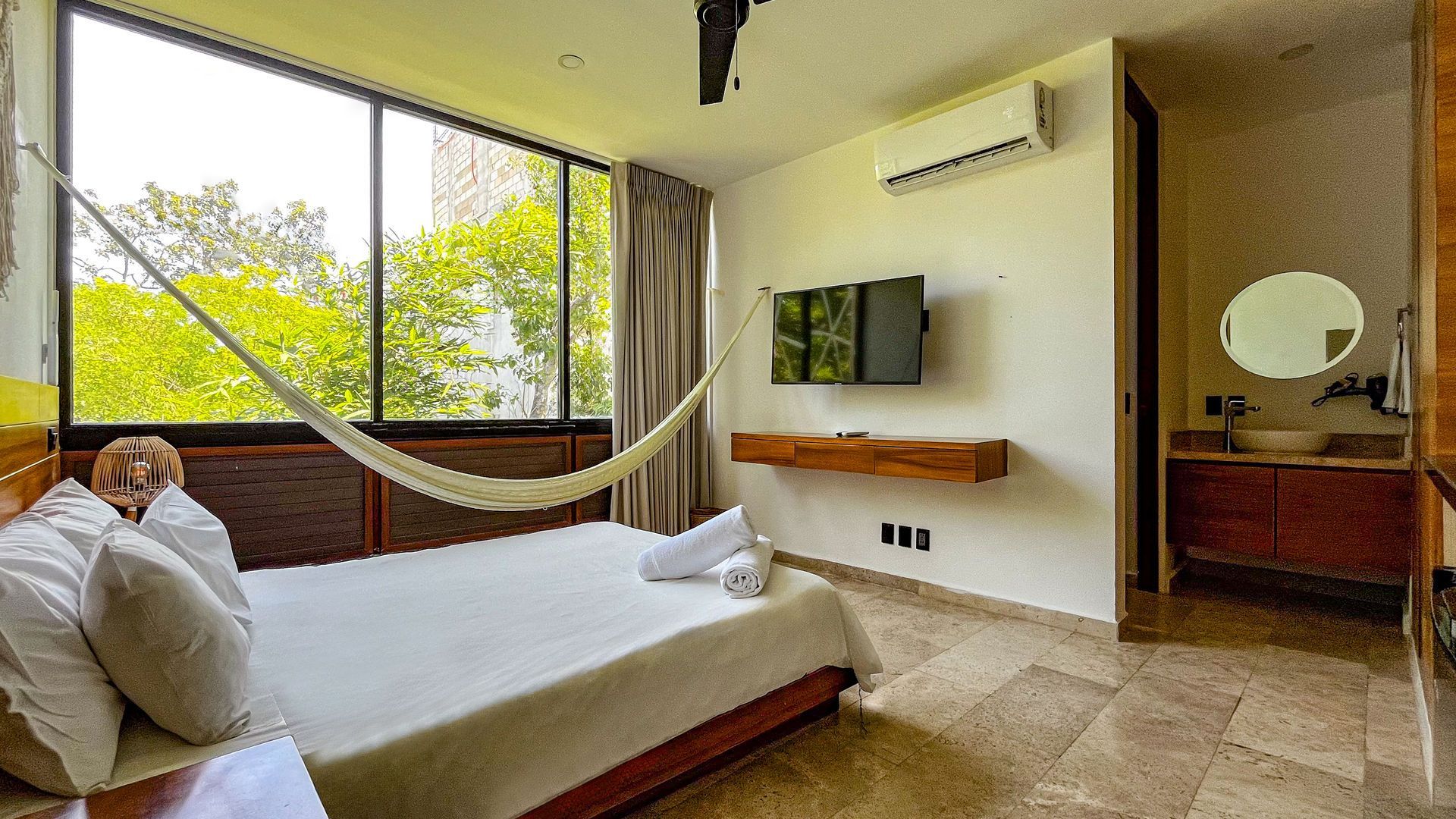 Dormitorio con cama, hamaca, TV, ventana y baño.