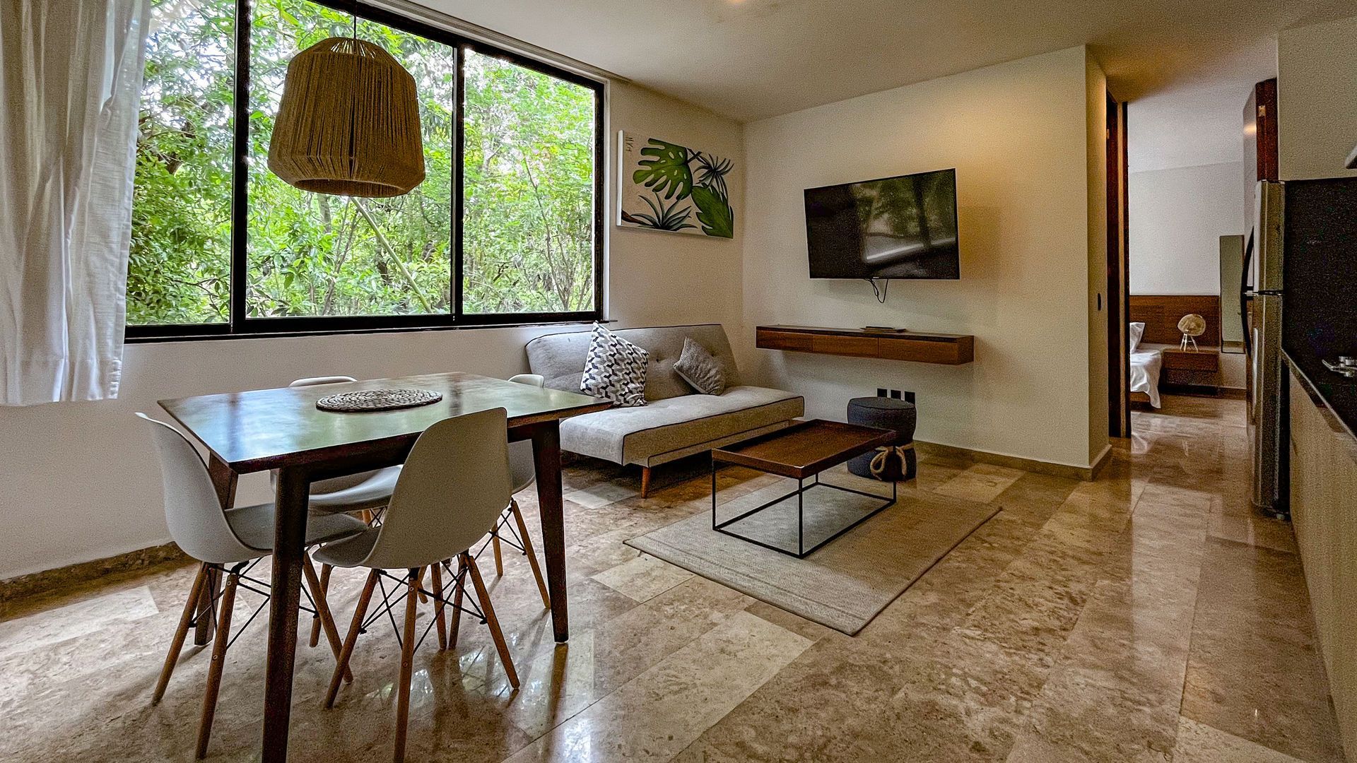 Apartamento moderno con sala de estar, comedor, sofá, TV y vista a la vegetación fuera de la ventana.