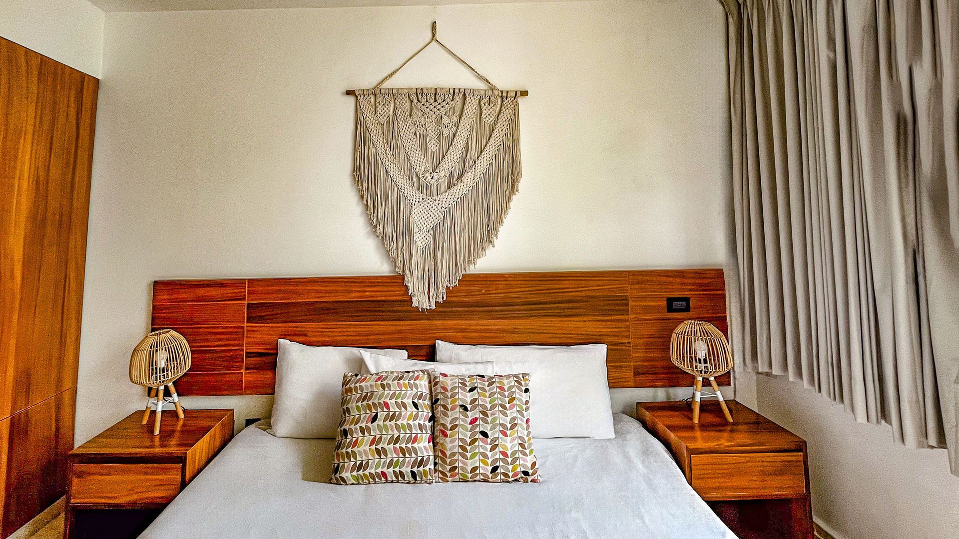 Dormitorio con cabecero de madera, tapiz de macramé y mesitas de noche con lámparas.