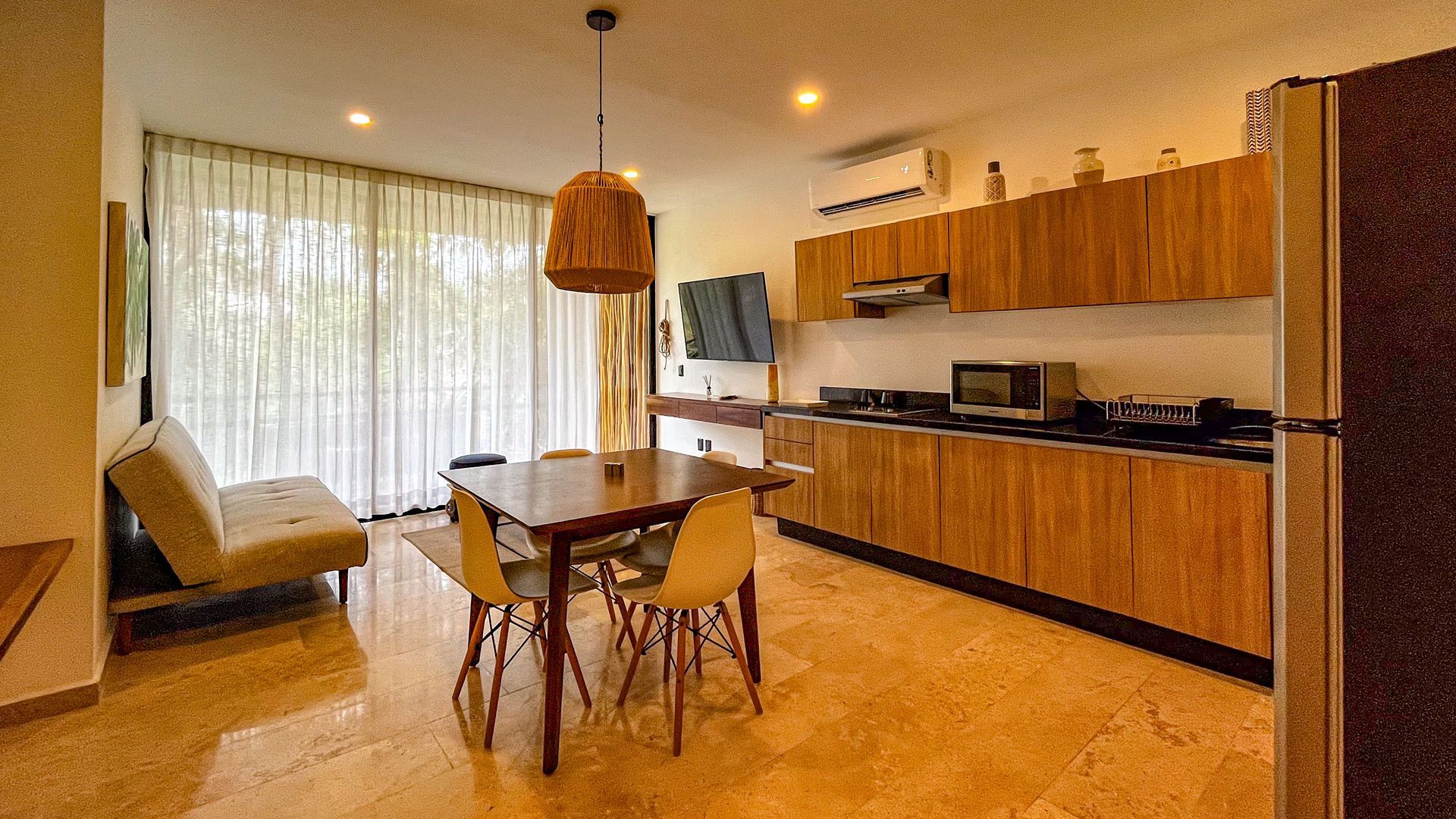 Cocina-comedor de planta abierta con gabinetes de madera y mesa de comedor; ventana grande con cortinas.