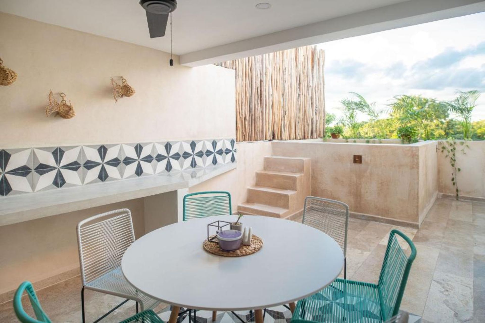 Patio al aire libre con mesa redonda, sillas de colores, mostrador incorporado con azulejos estampados y pequeños escalones.