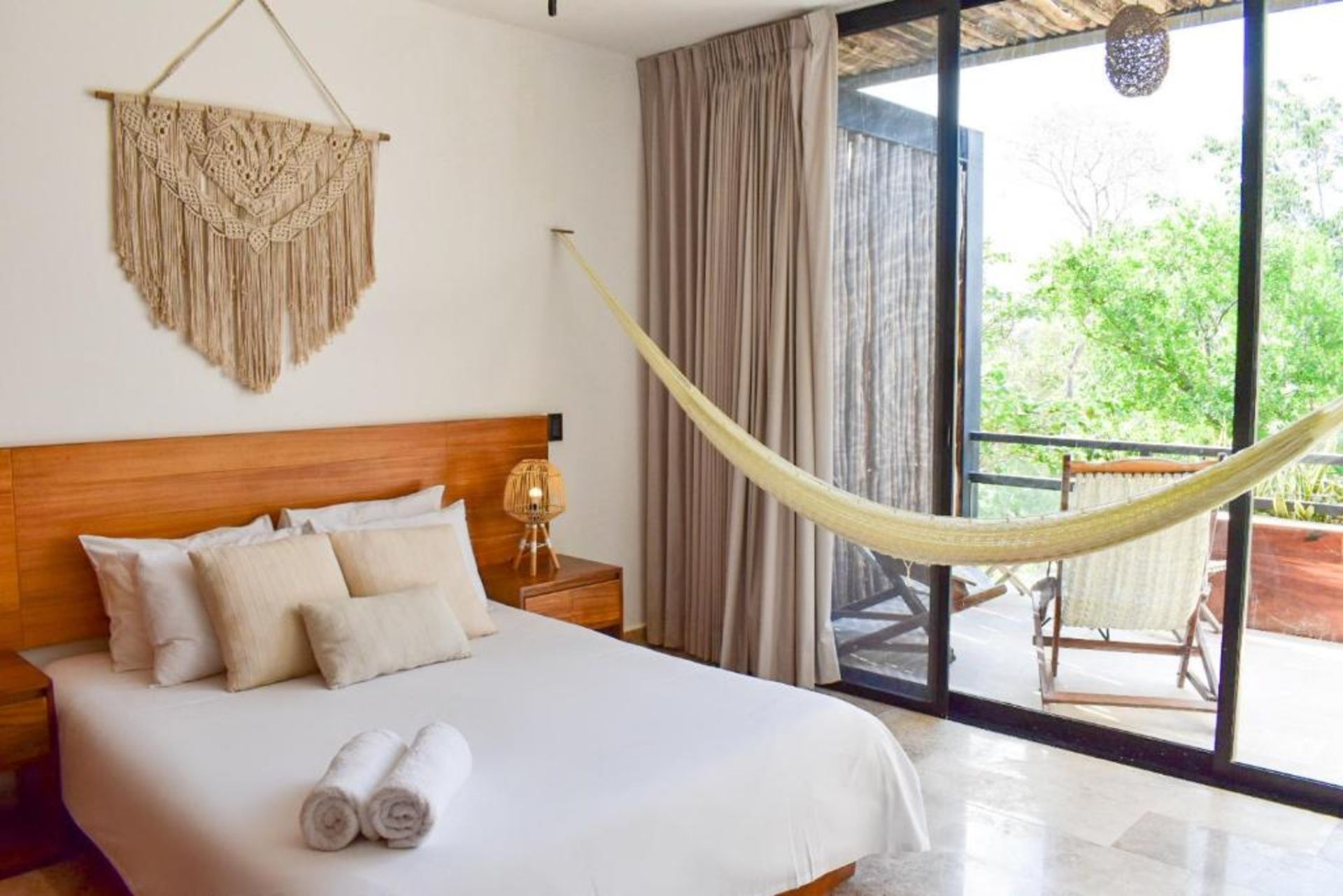 Dormitorio con cama, tapiz de macramé, hamaca y balcón con silla.
