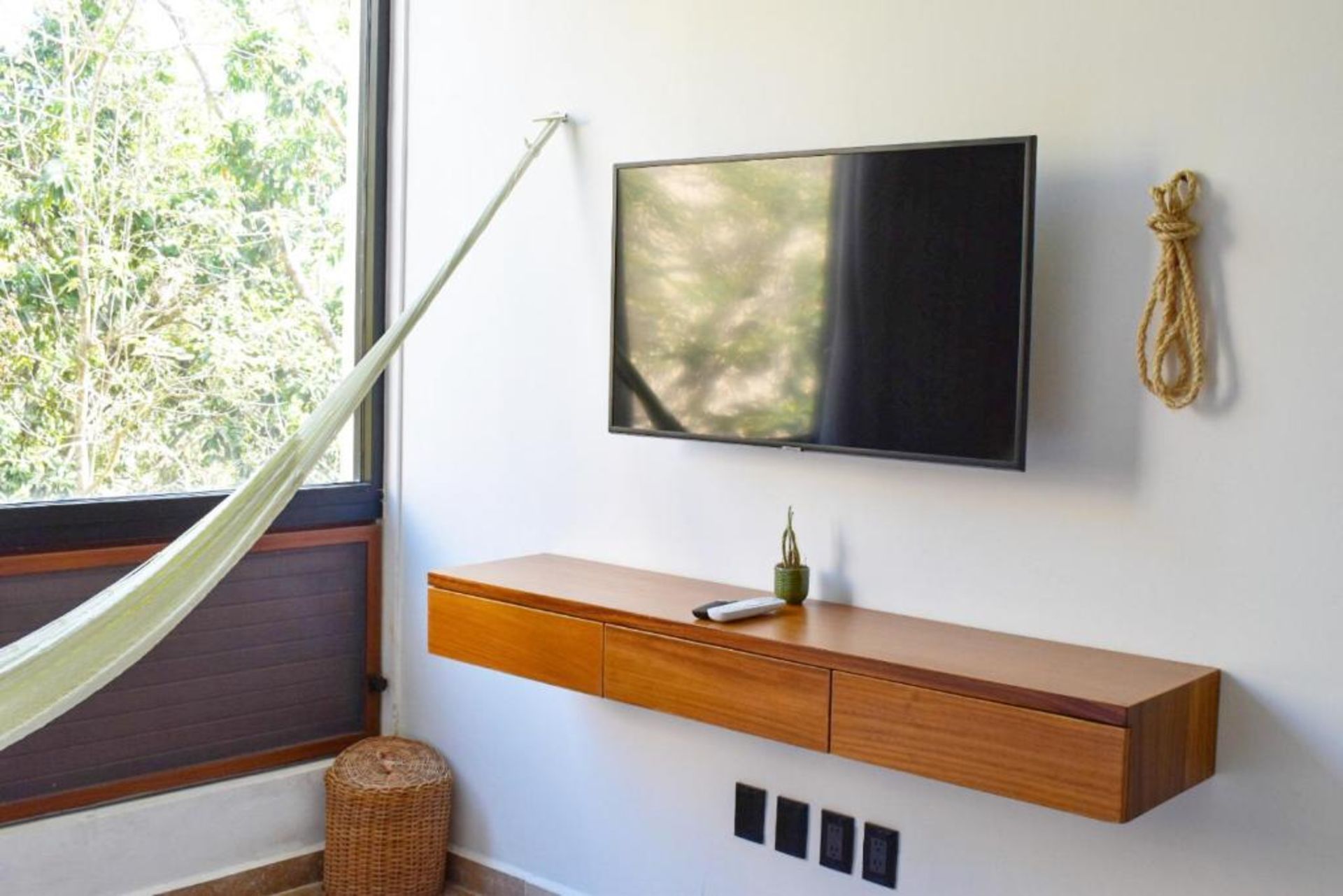 Moderna sala de estar con TV de pared, consola de madera y hamaca cerca de una ventana.