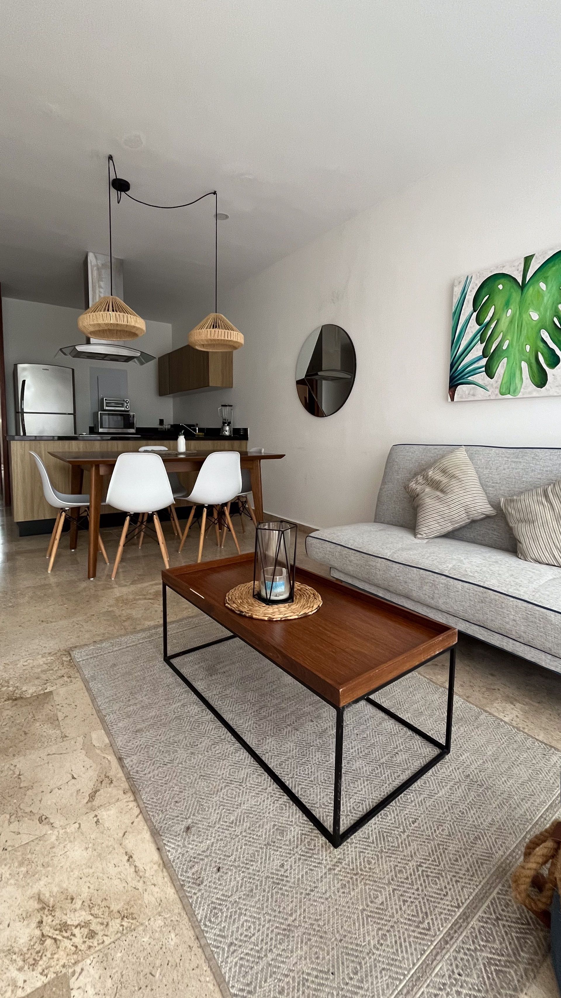 Sala de estar con decoración moderna, una mesa de centro de madera y una pequeña cocina visible al fondo.