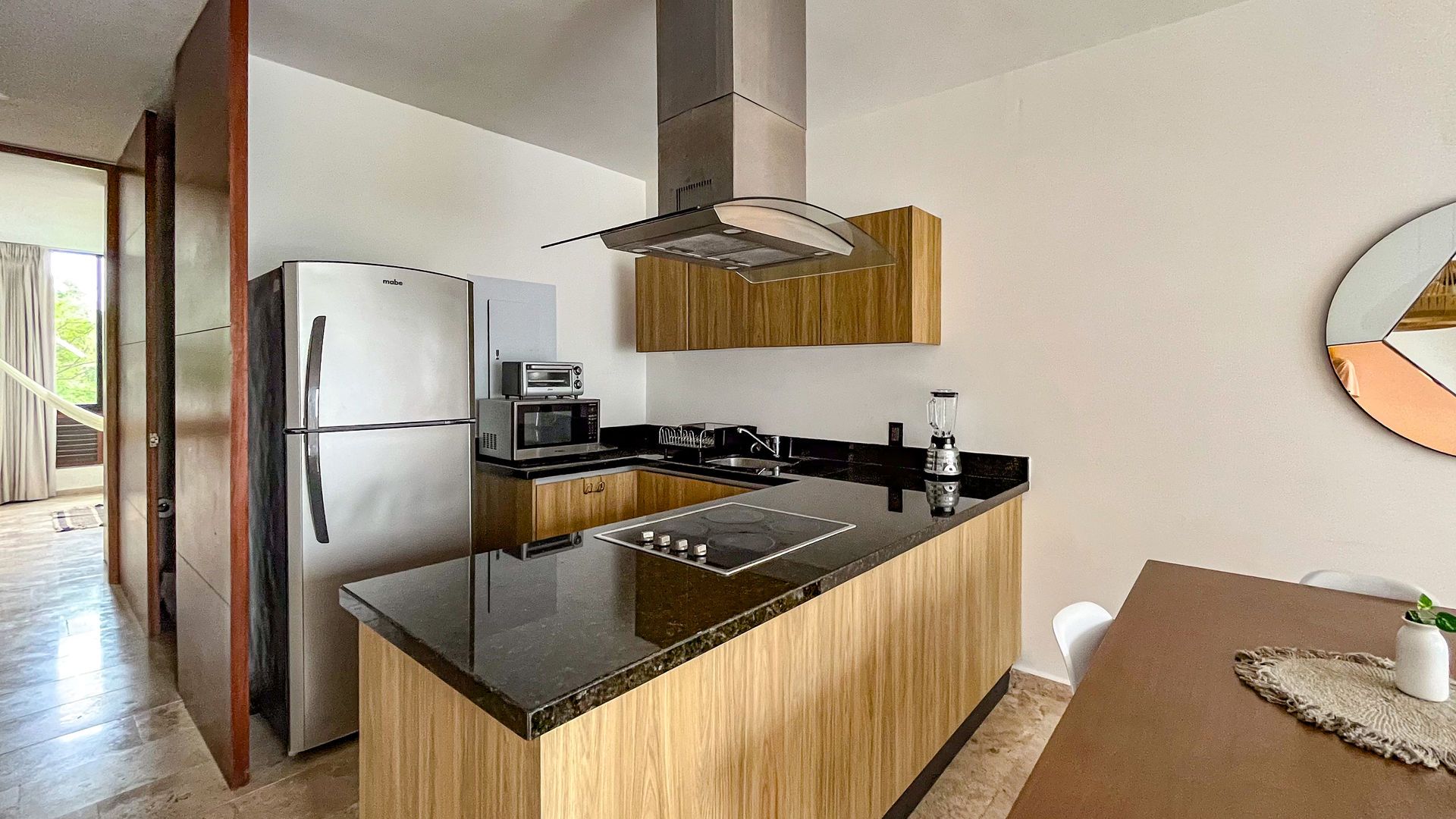 Cocina moderna con electrodomésticos de acero inoxidable, encimera negra, gabinetes de madera y un espejo decorativo.