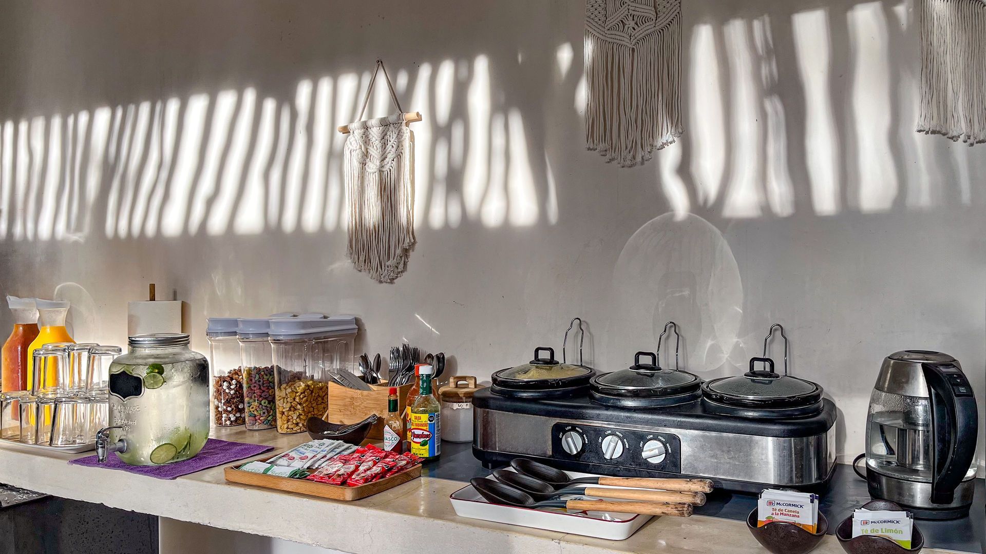 Buffet con comida y bebidas en un mostrador, sombras de la luz del sol en la pared.
