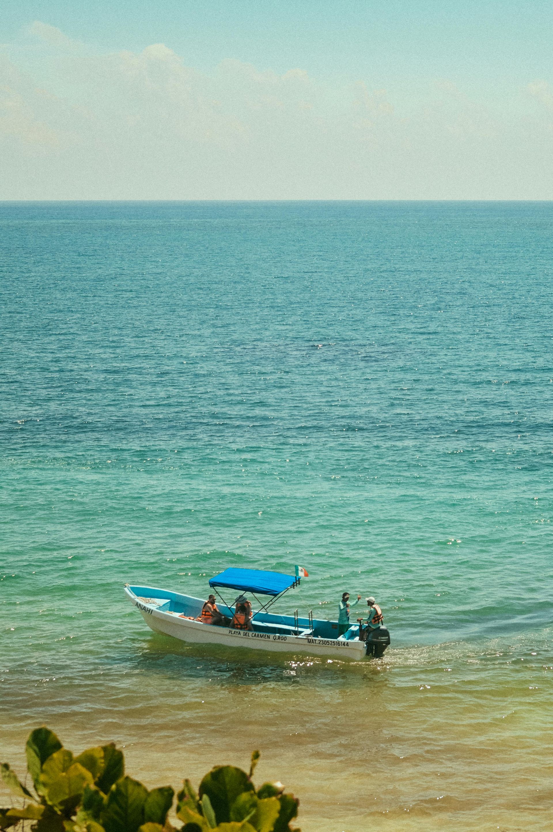 Un barco con dosel azul flota en aguas turquesas claras cerca de una playa de arena.